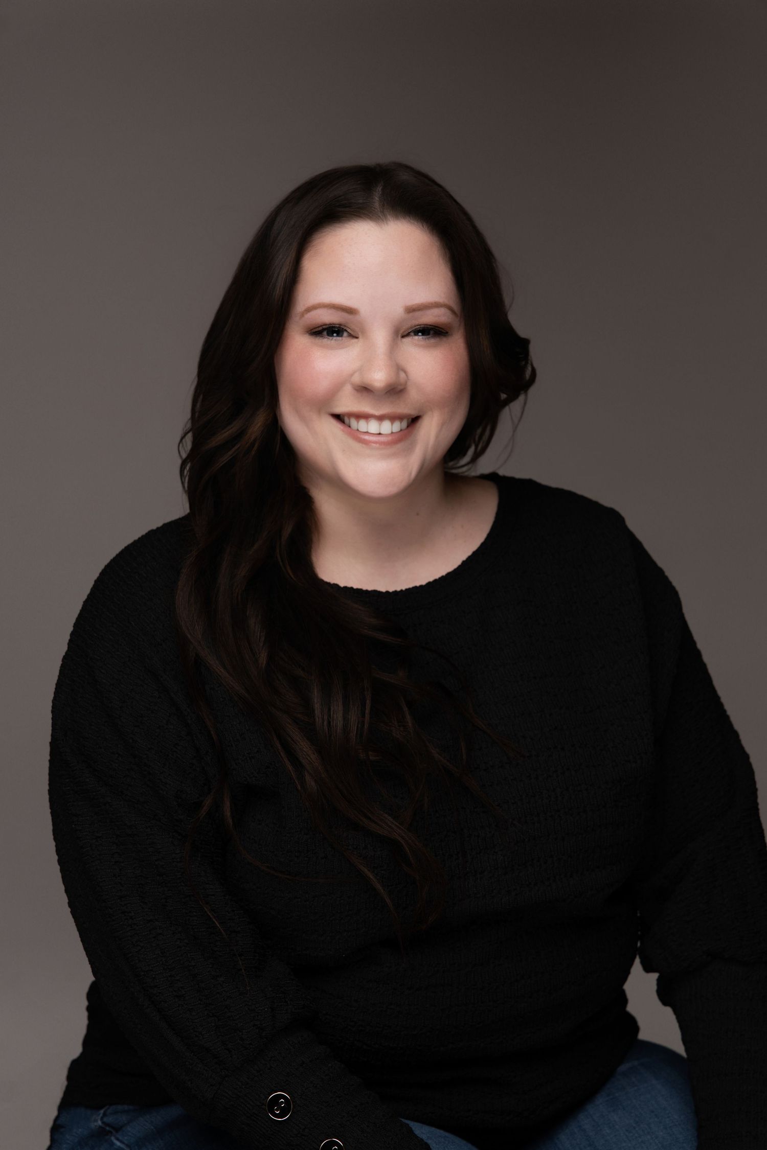 Studio portrait of woman in black sweater against dark background.