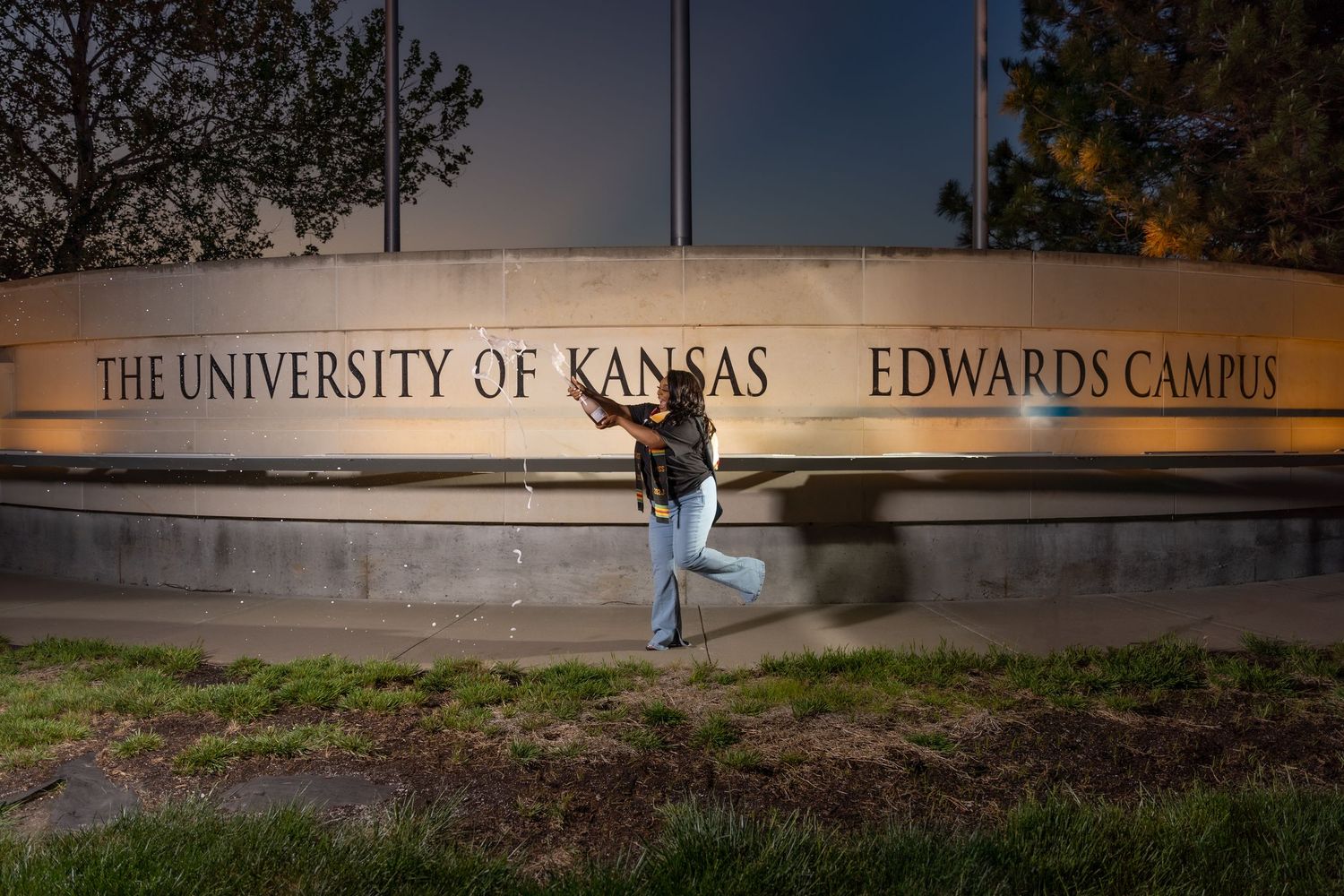 A celebratory pose in front of the University of Kansas Edwards Campus sign at dusk.