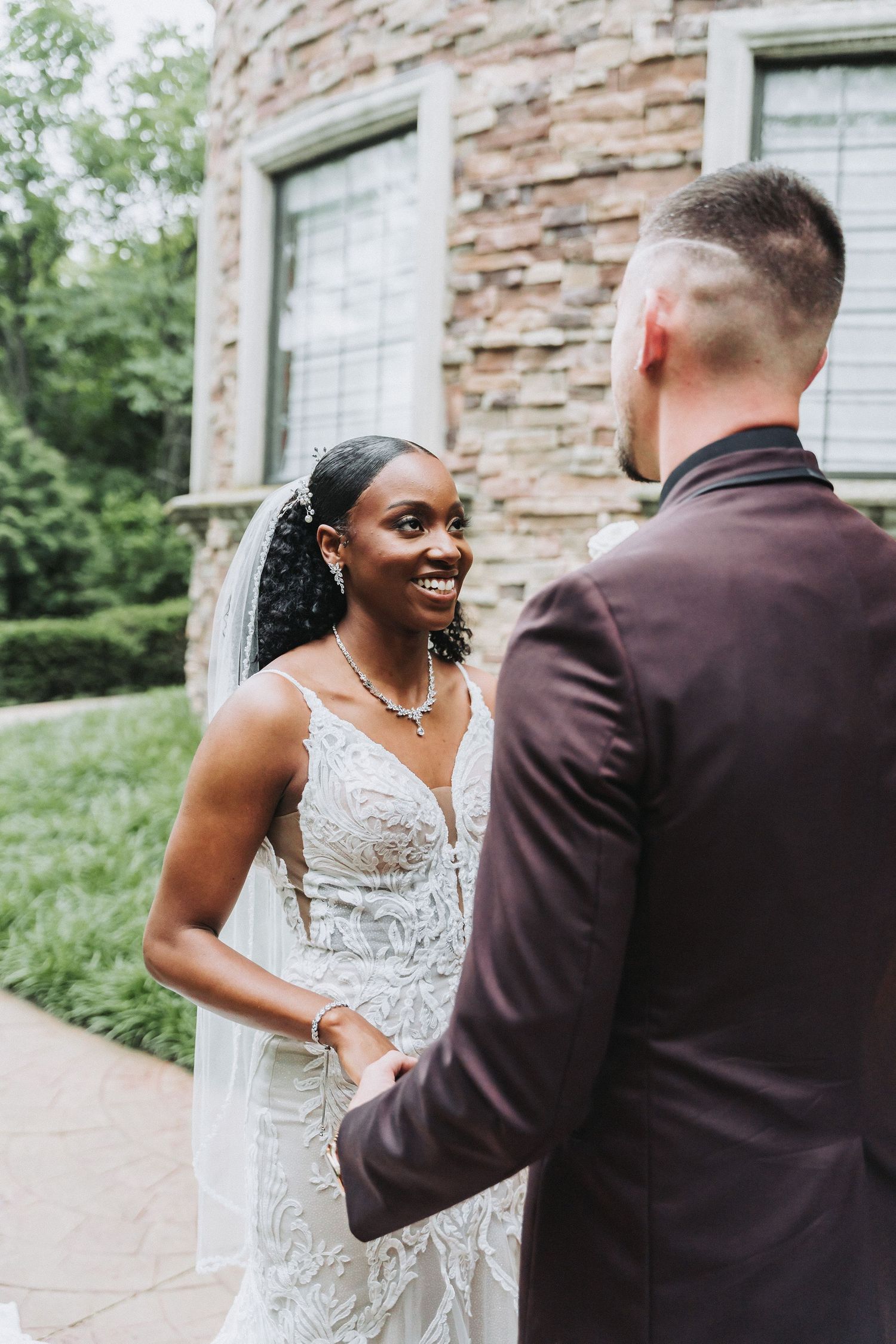 Joyful bride in lace gown shares first look moment with groom outside stone building.