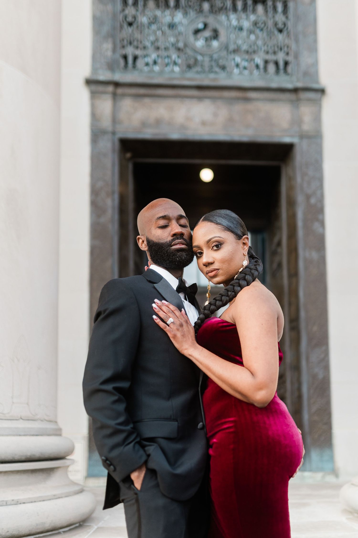 Close-up portrait of couple in formal attire embracing by classical architecture.