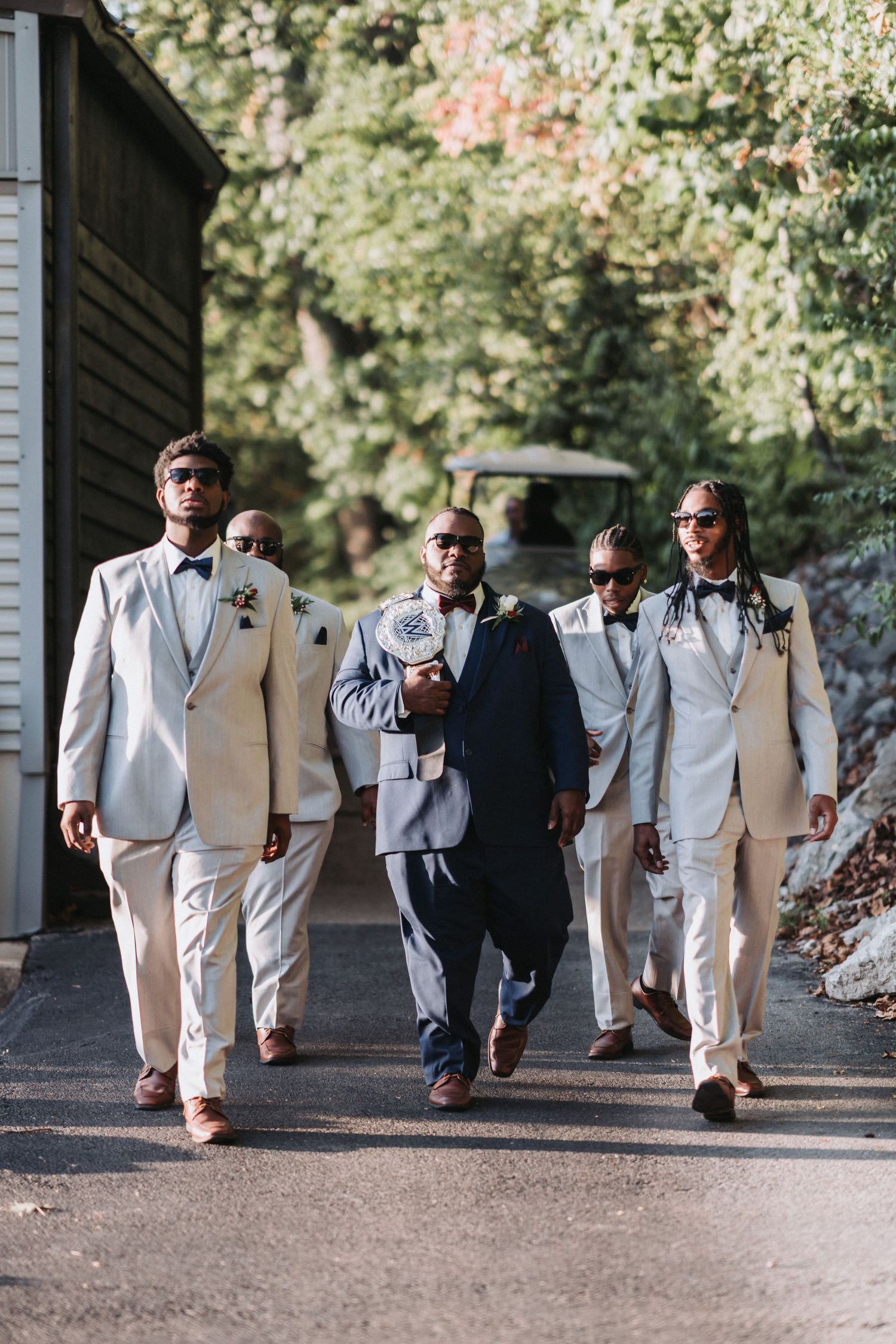 Groomsmen in light colored suits walk confidently down a path.