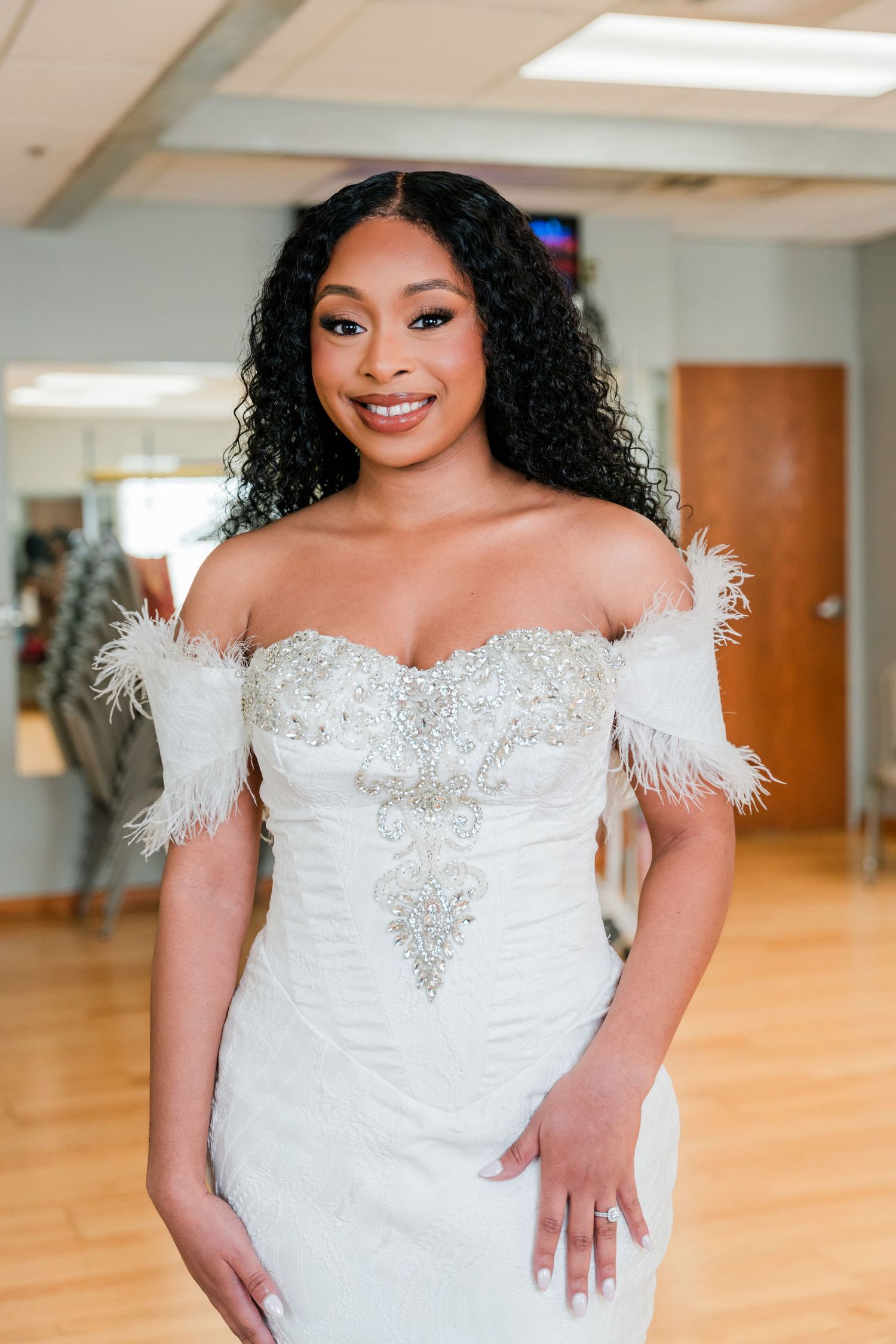 Stunning off-shoulder white wedding gown with feather details and beaded embellishments.