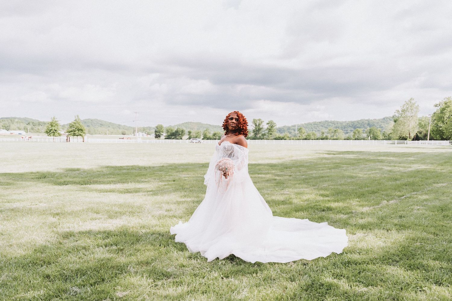 Back view of bride in flowing white dress standing in open field.