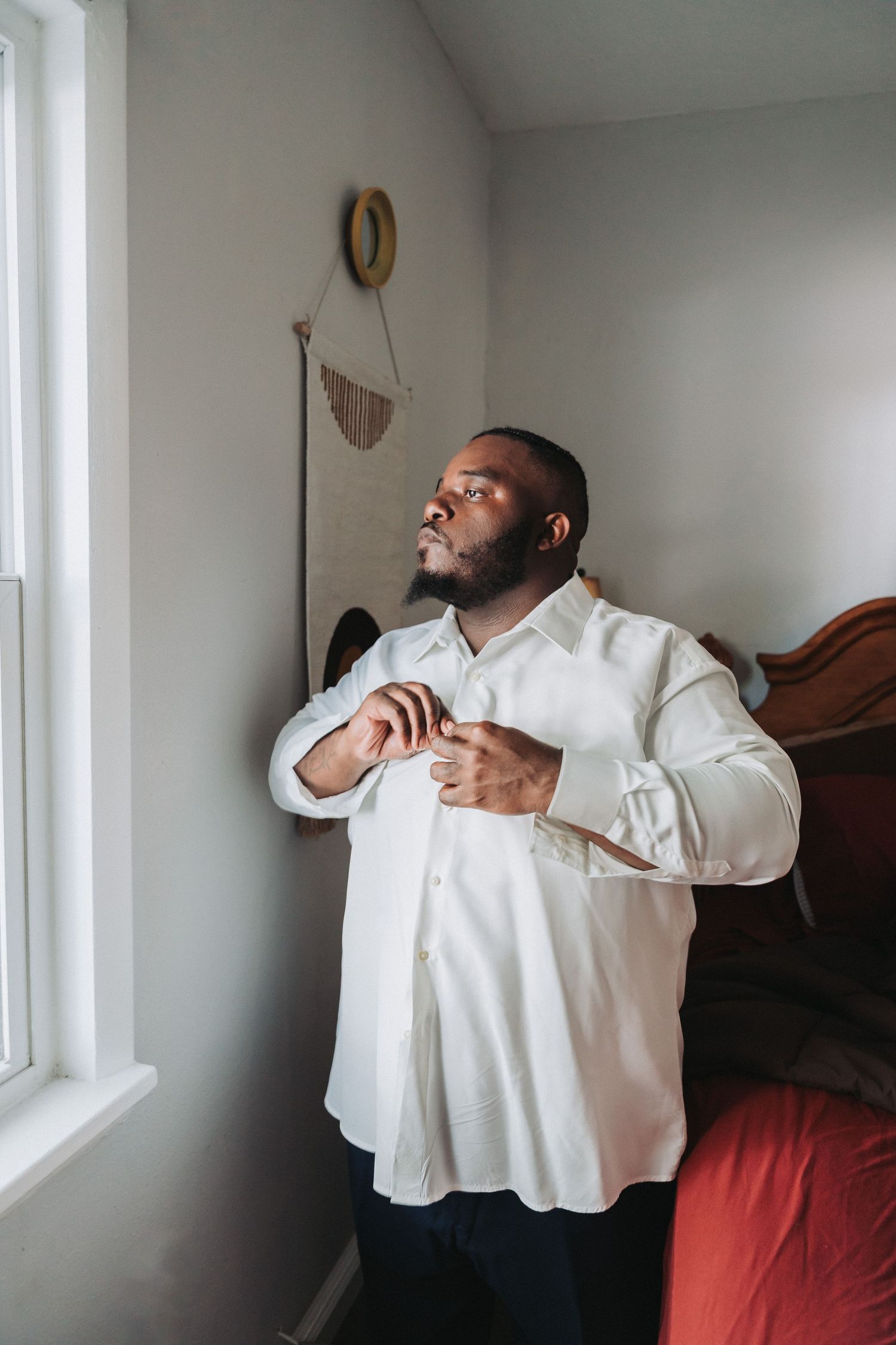 A person in white dress shirt adjusting their collar while standing by a window.