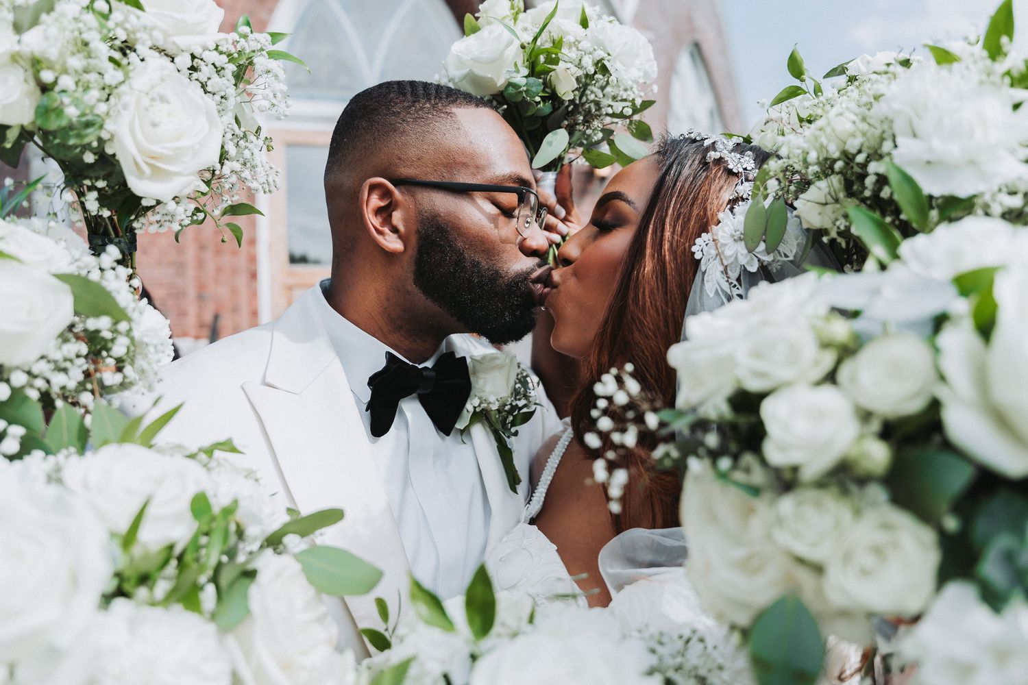 A romantic wedding scene with white floral decor as newlyweds share a kiss.
