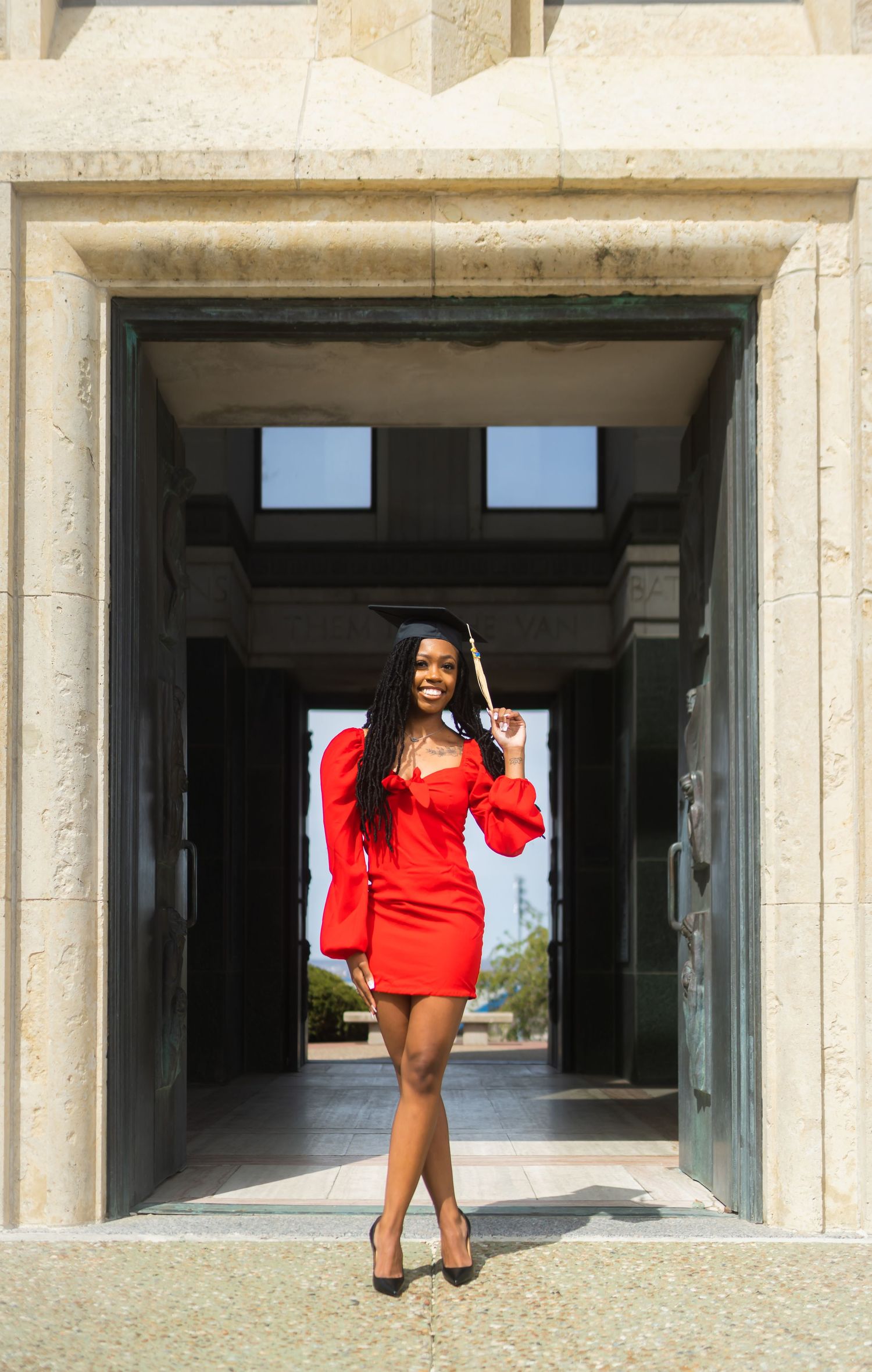 Graduate in red dress poses in stone archway during graduation photoshoot.