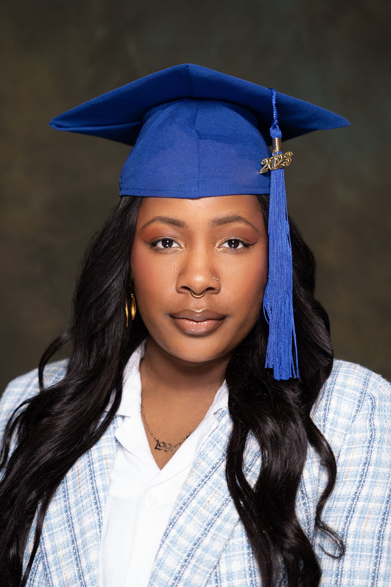 Graduate in blue cap with tassel poses for professional portrait in checkered outfit.