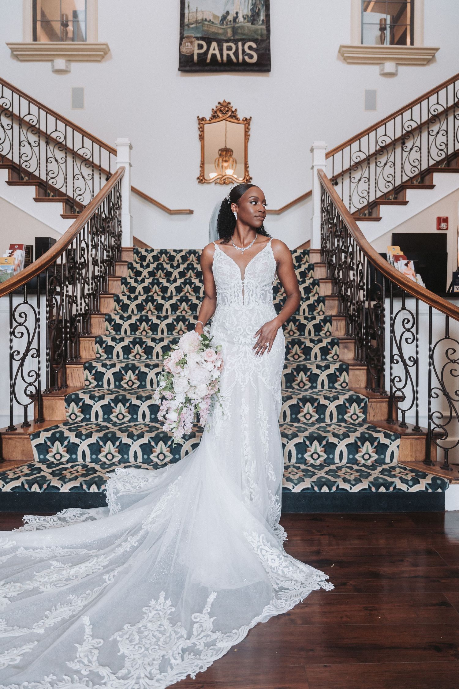 Elegant bride poses on grand staircase with ornate black and white carpet and Paris artwork in elegant venue.