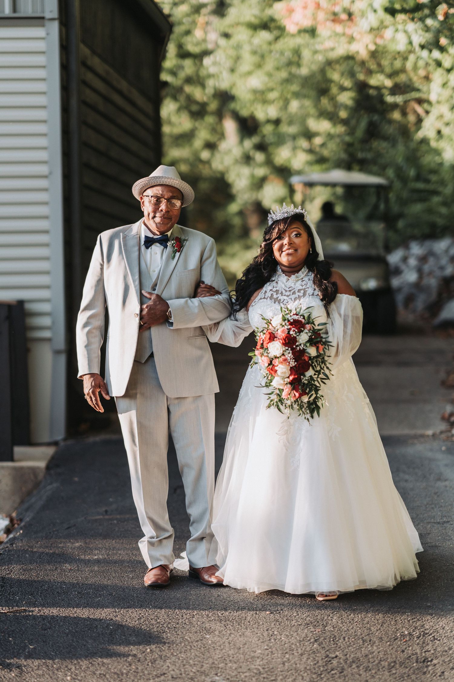 A couple in formal wedding attire walk together while holding a beautiful floral bouquet.