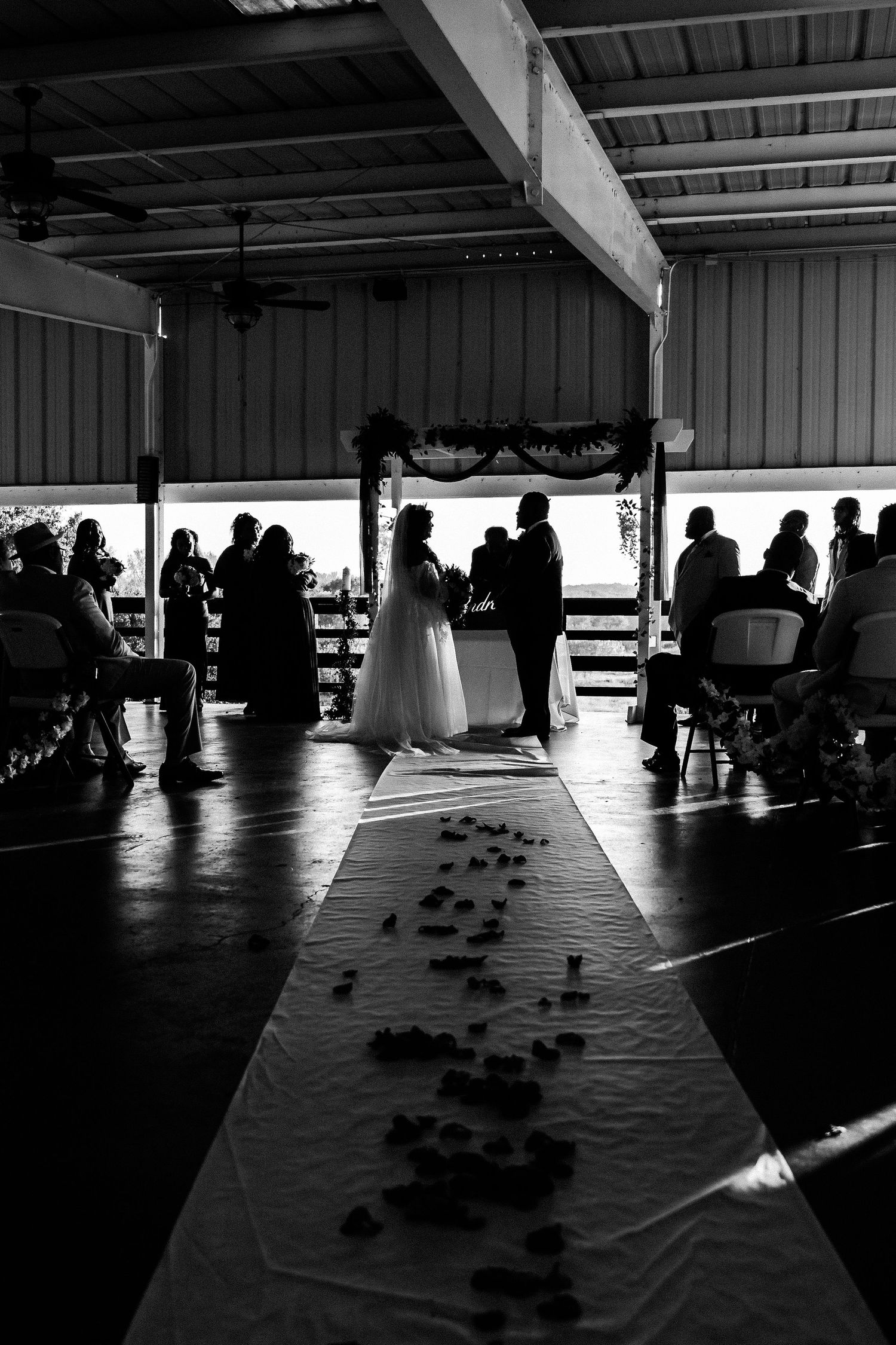 Black and white photo of a wedding ceremony silhouetted under a covered pavilion.