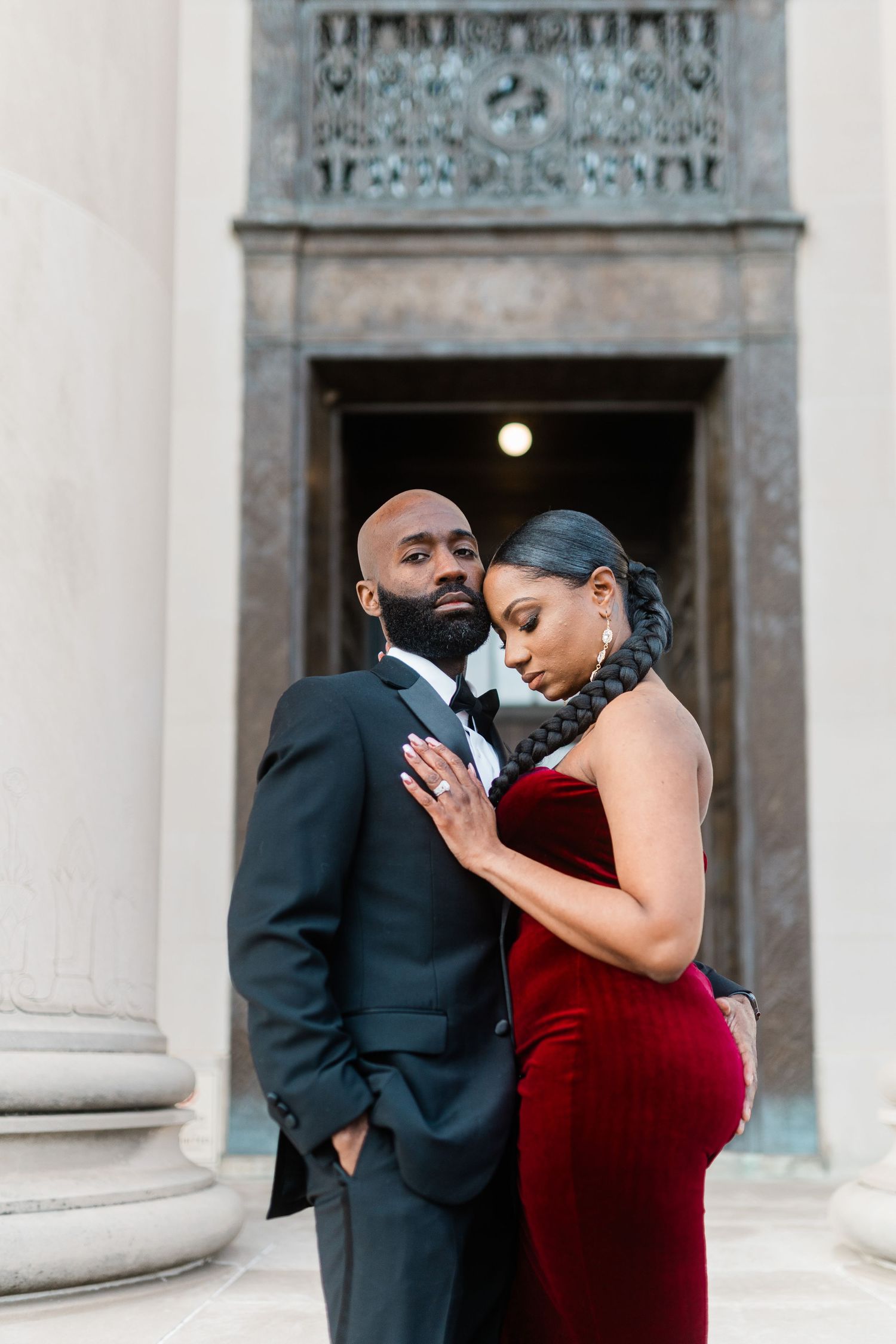 Intimate portrait of couple in formal wear standing by ornate doorway and stone columns.