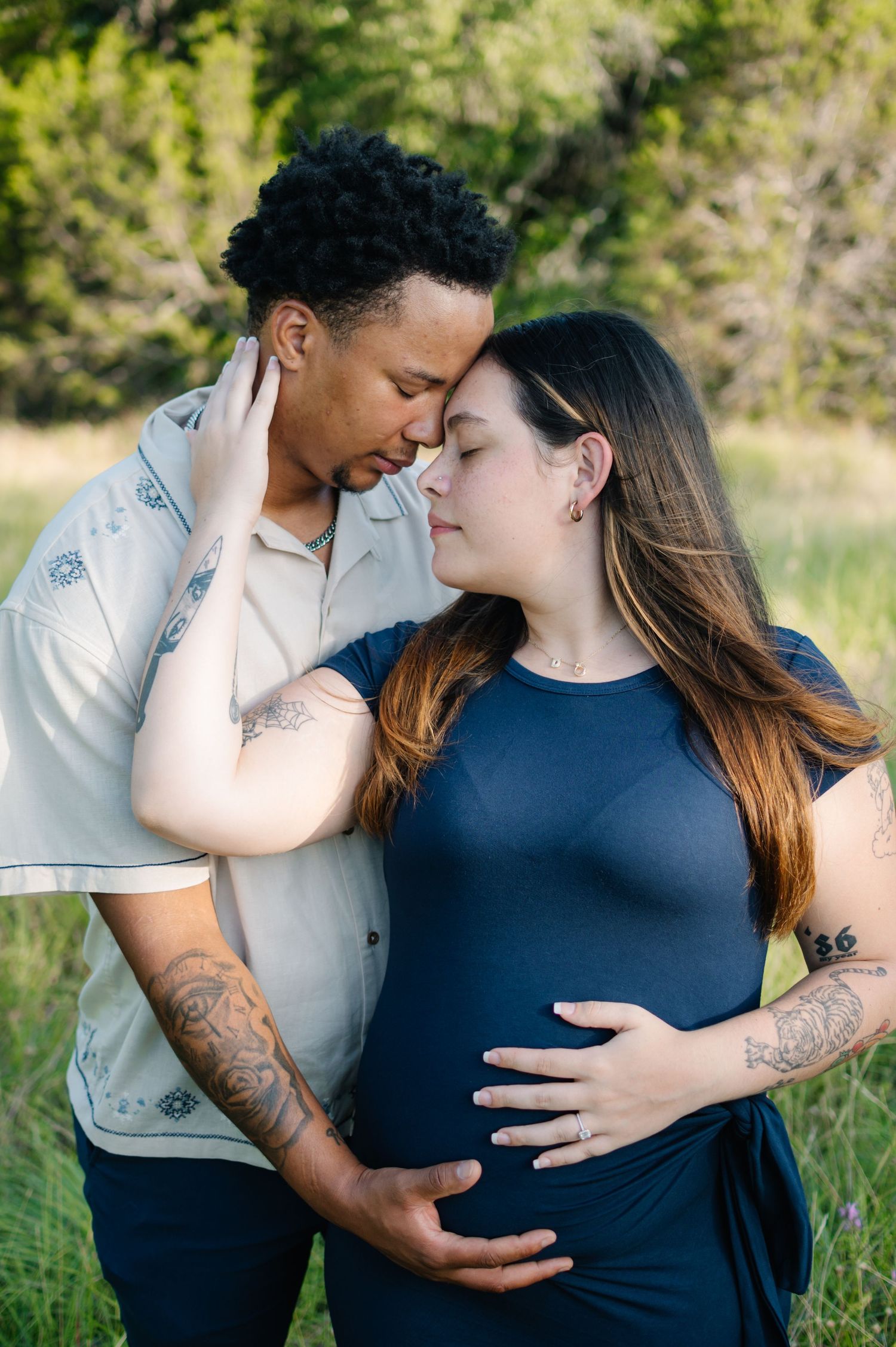 A couple shares intimate moments in a natural outdoor setting wearing navy and white clothing.