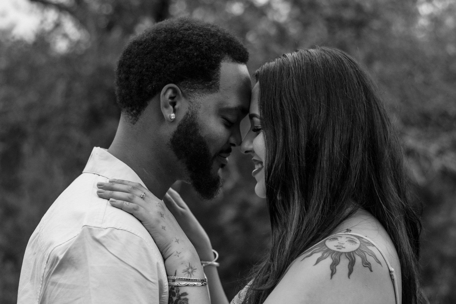 Black and white photo of a smiling couple sharing a romantic moment, touching foreheads outdoors.