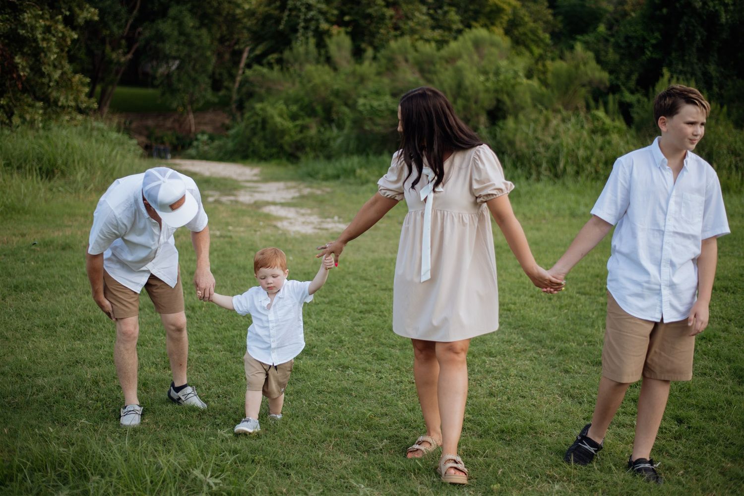 Family walking together through a green grassy meadow on a sunny summer day, holding hands in a line.