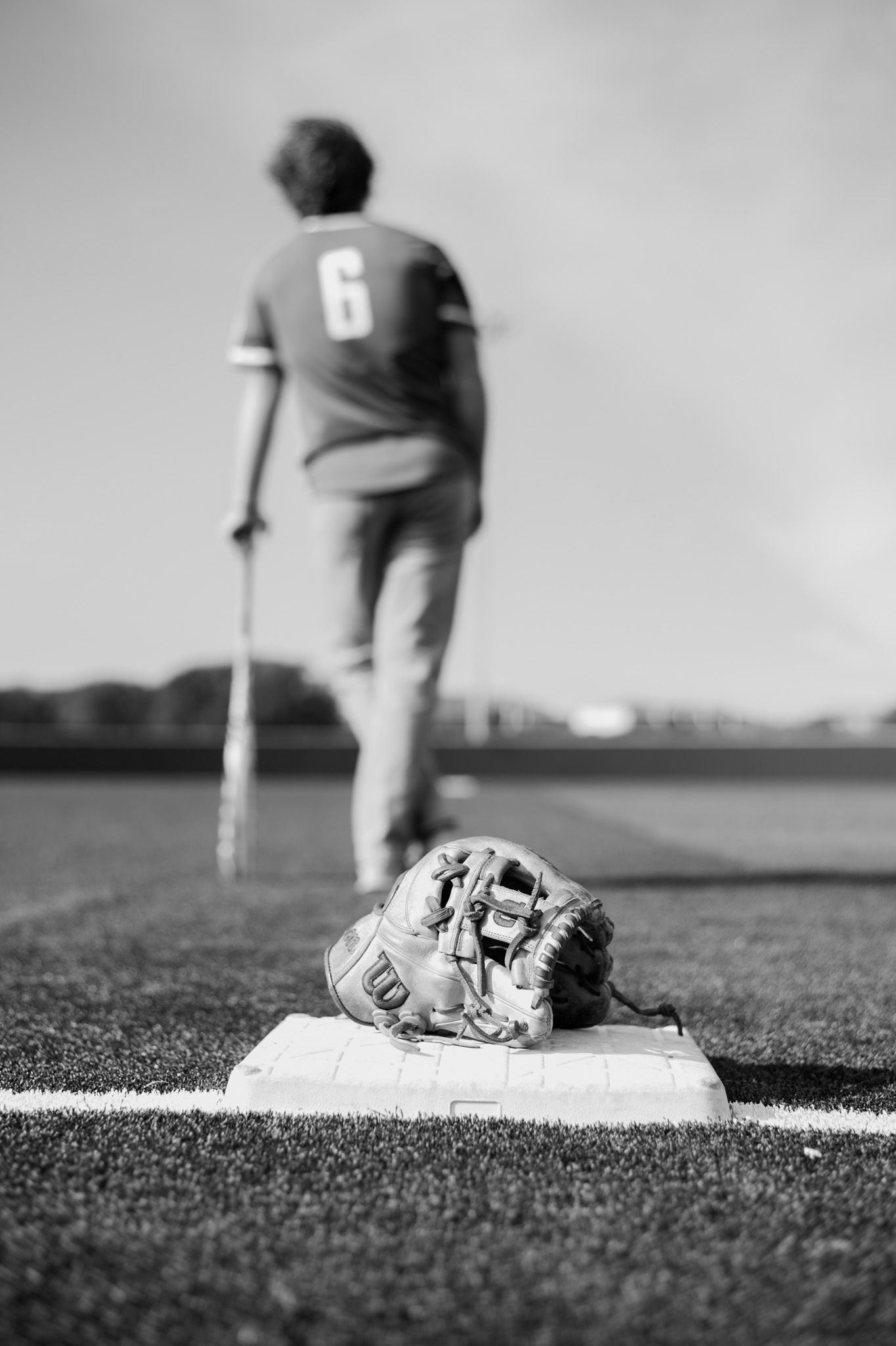 Black and white photo of baseball glove on base with player number 6 holding bat in background.