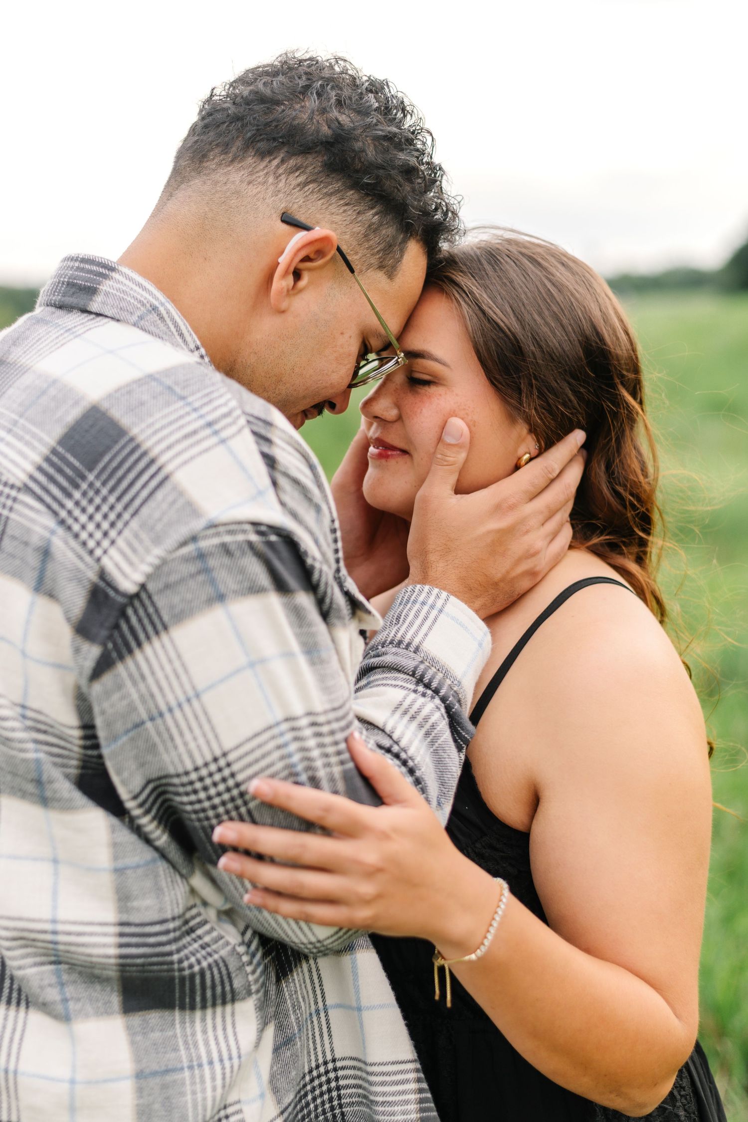 Couple sharing a tender forehead-to-forehead moment outdoors, man in plaid shirt gently cupping woman's face.