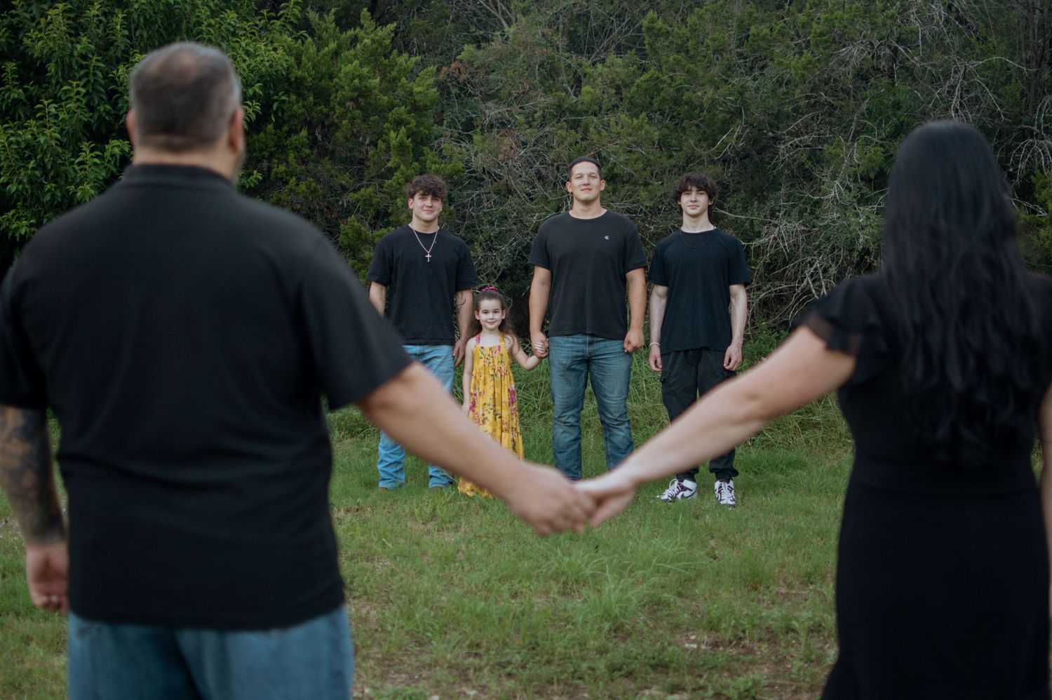 A group in black t-shirts poses together on a grassy lawn while two people are seen from behind holding hands.
