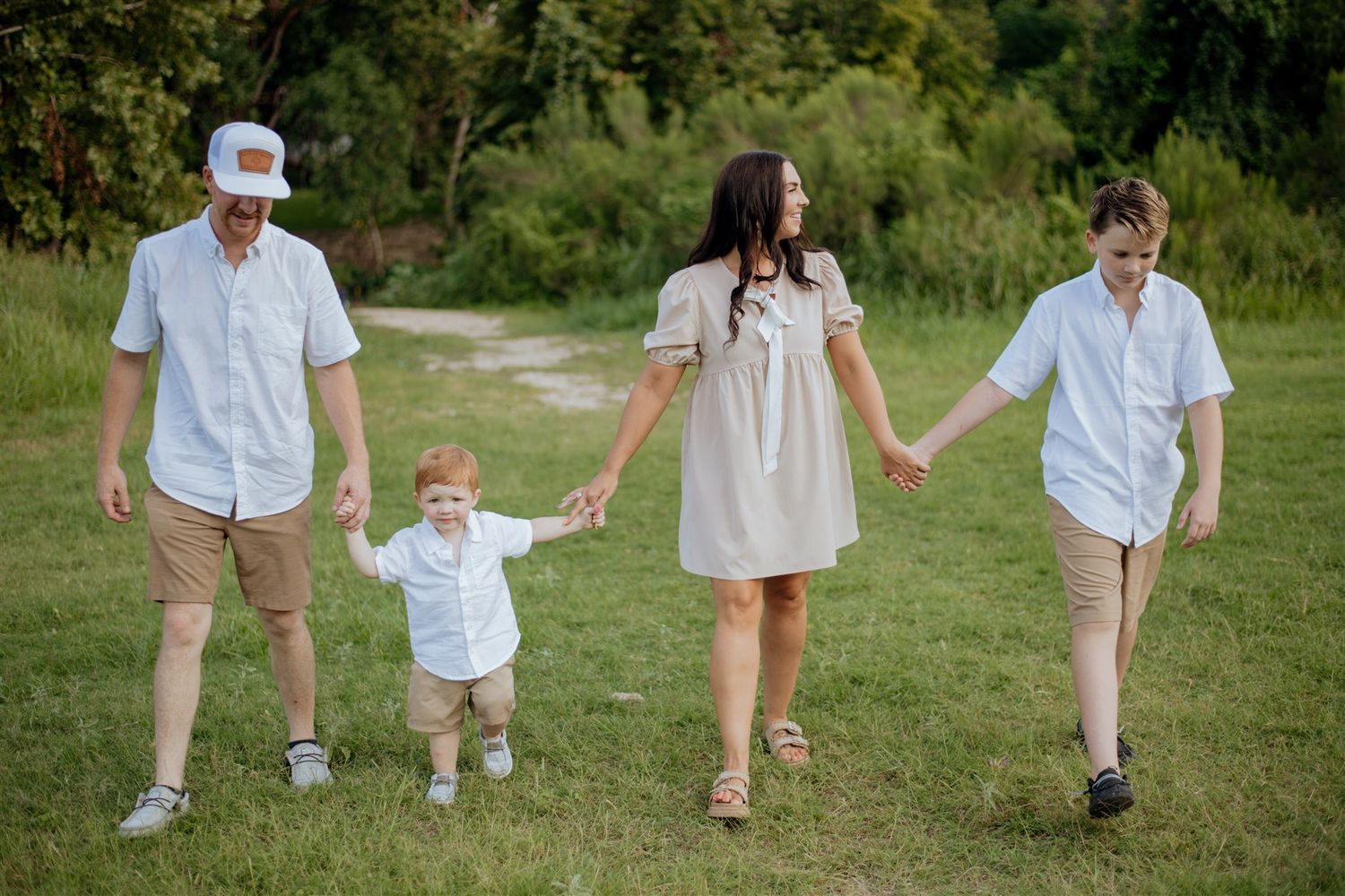 A family walks together holding hands across a sunny green field on a summer day.