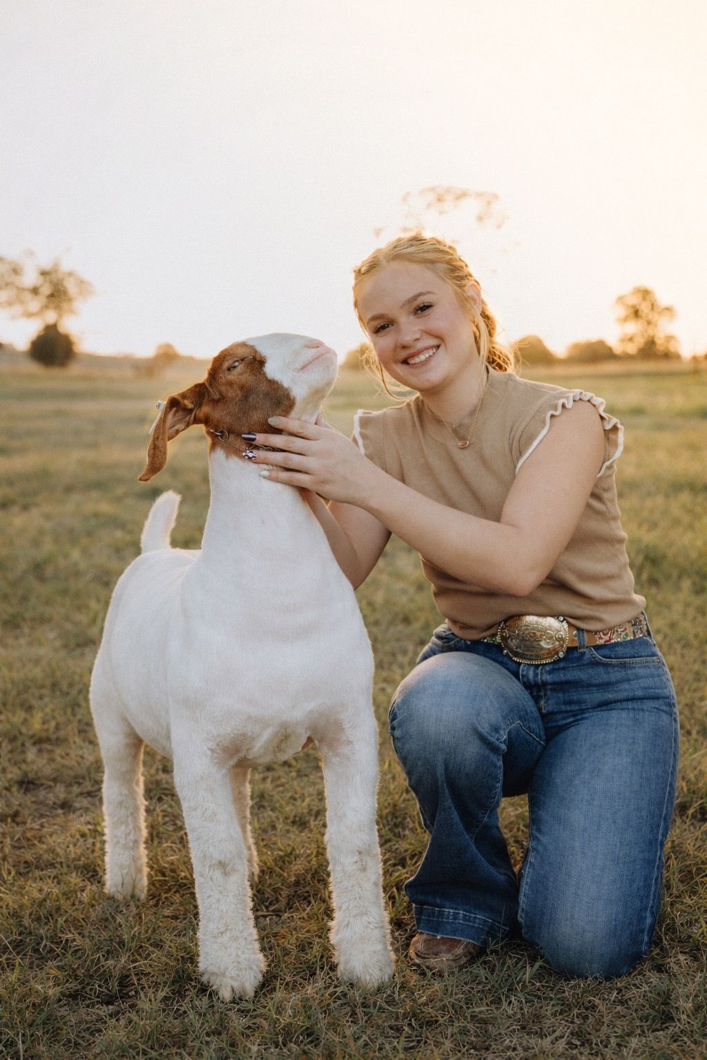 A young goat and person in casual wear share a playful moment in a sunlit field at golden hour.
