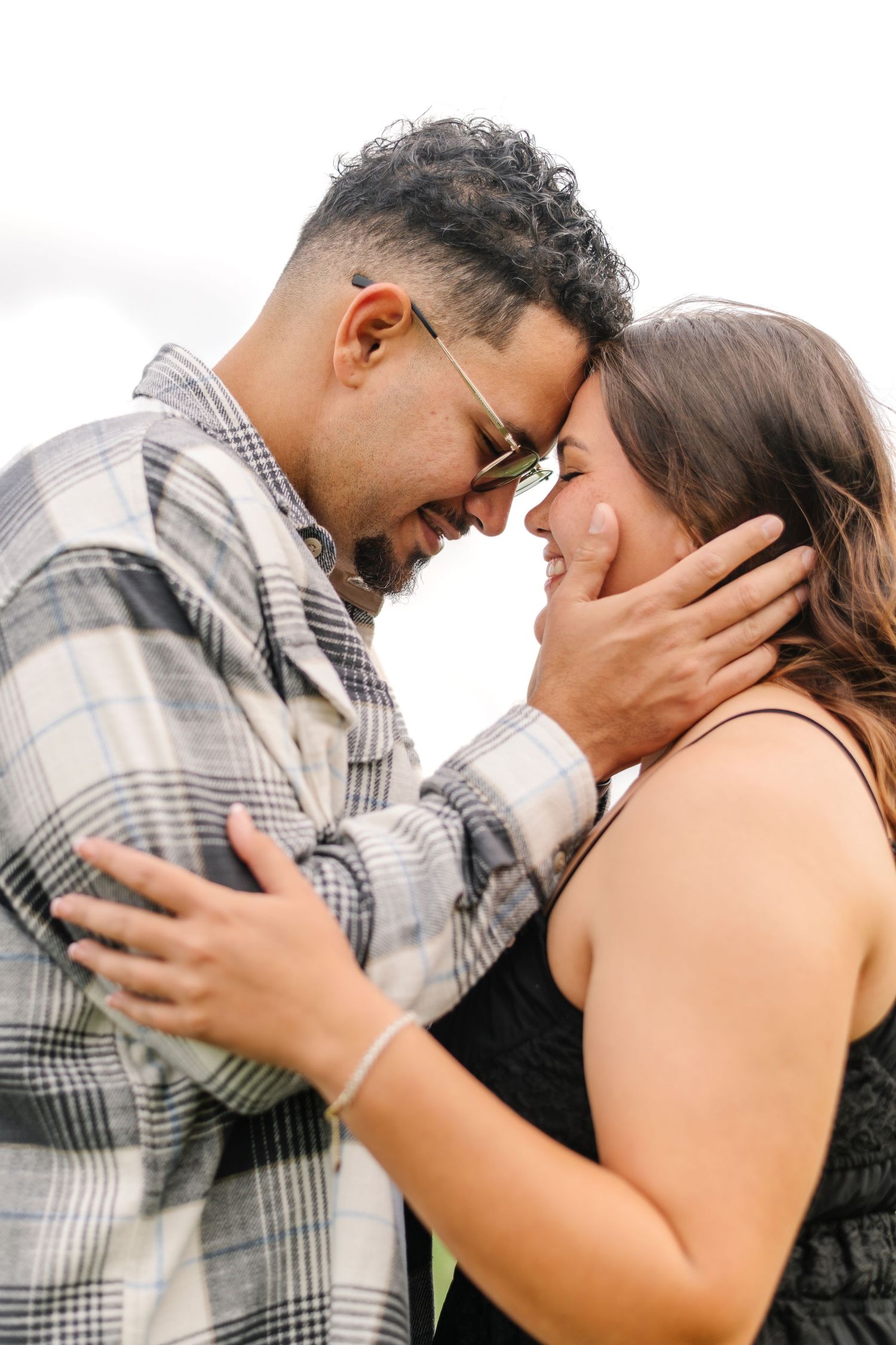 A couple shares a tender moment, foreheads touching and smiling, as the man gently cups the woman's face.