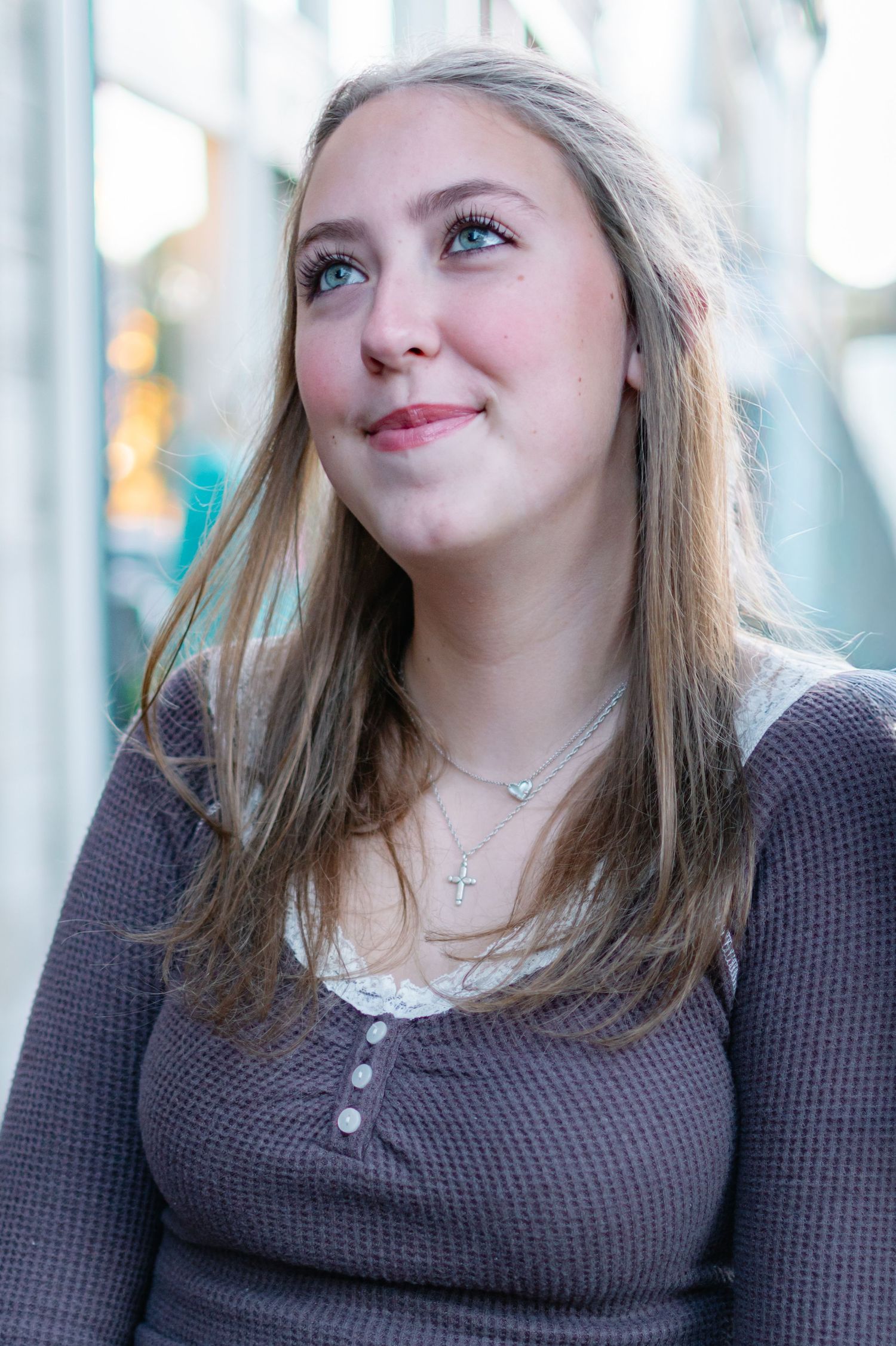 Portrait of someone with long blonde hair wearing a gray sweater looking up with a gentle smile.