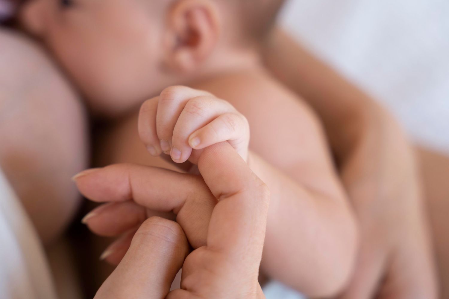 A baby breastfeeding while holding the mothers finger