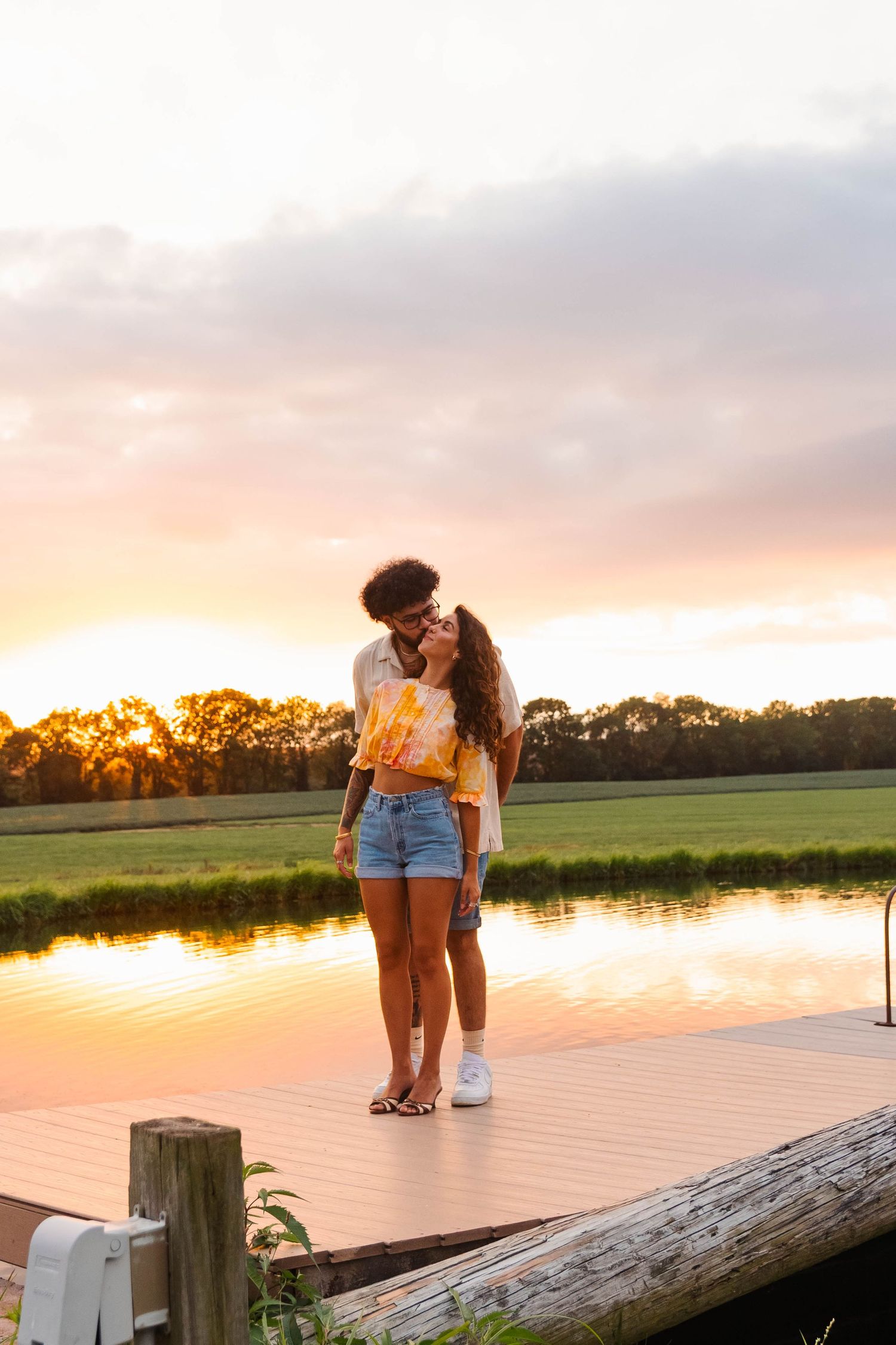Couple embracing on a wooden dock at sunset with golden reflections on a calm pond in Elverson, PA.