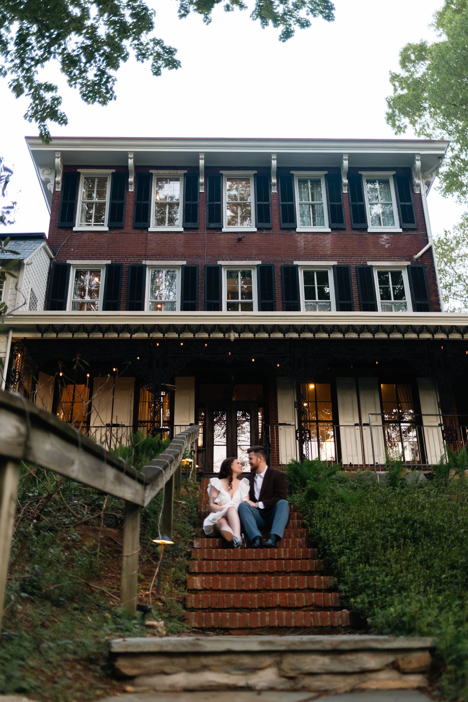 Couple sitting on brick steps in front of a charming historic red brick manor house in West Chester, PA.