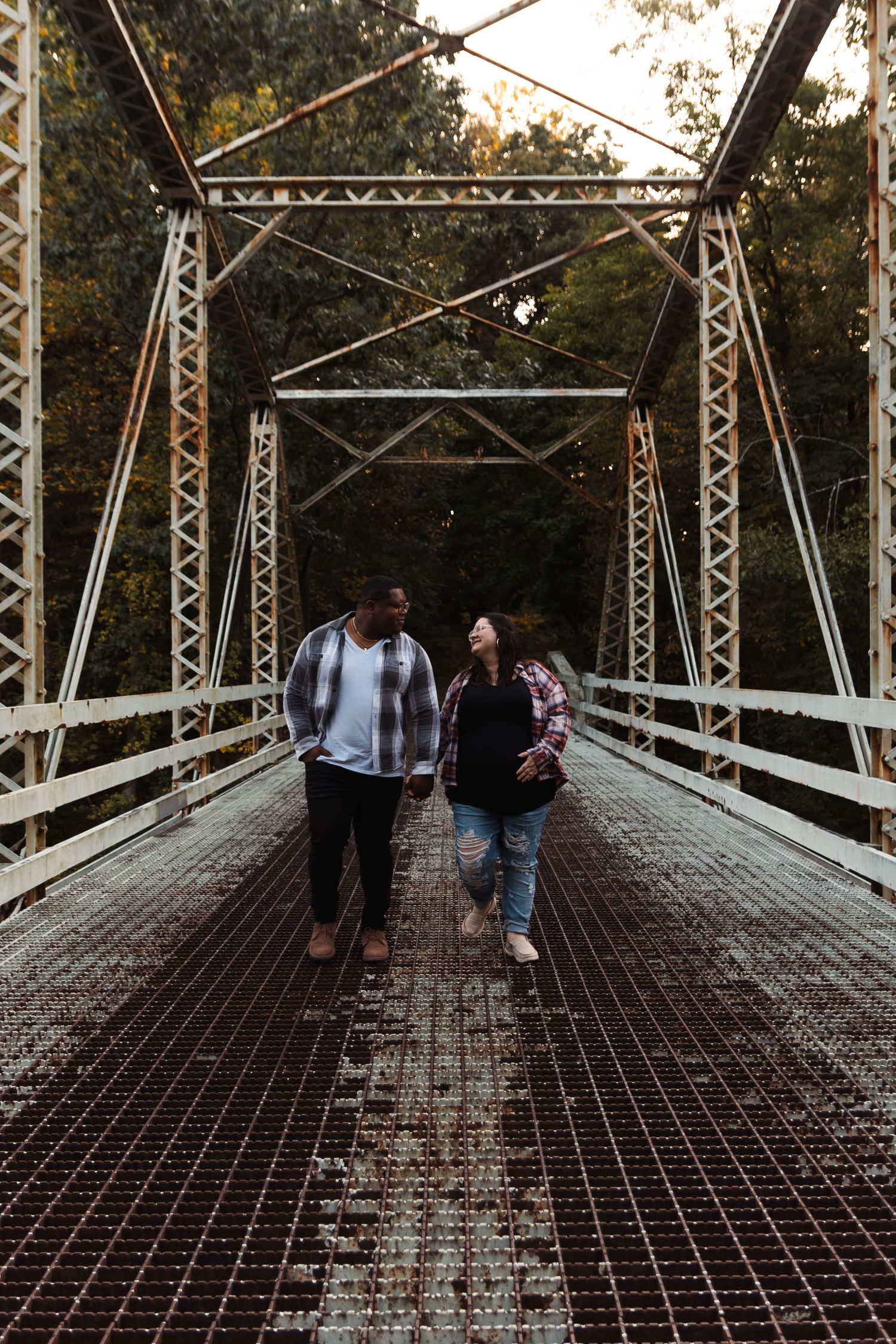 Interracial couple walking hand in hand across a rustic white iron bridge surrounded by autumn trees at Green Lane Park..