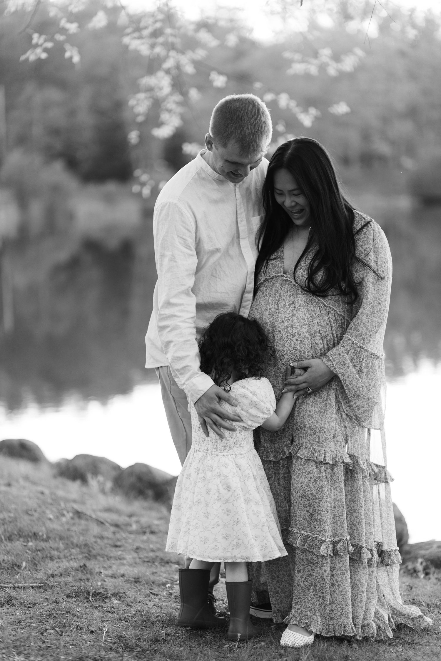 Black and white maternity photo of couple with toddler daughter touching pregnant belly at Green Lane Park.