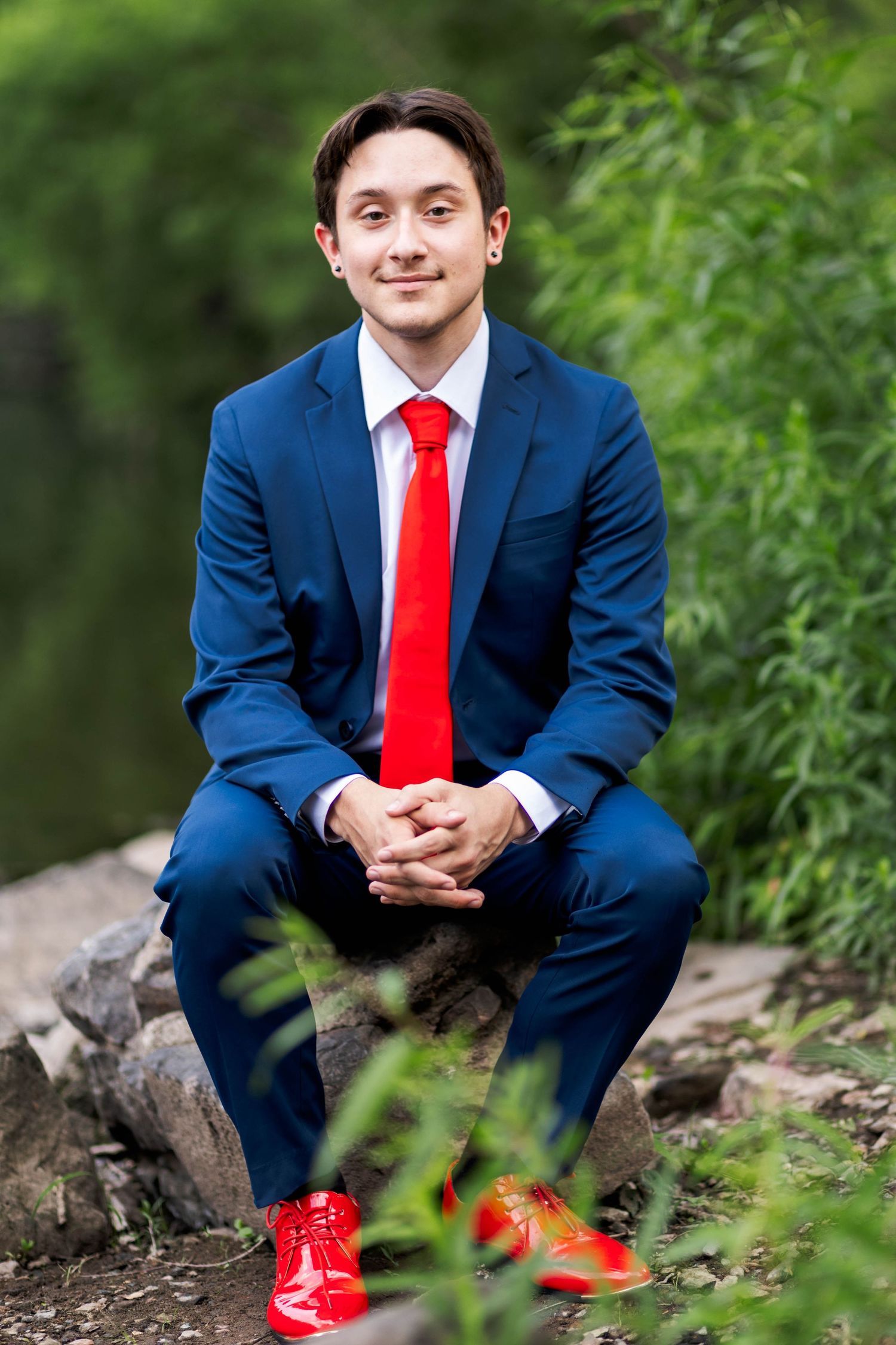 Owen J Roberts High School Senior in blue suit red tie and red shoes sitting on rocks outdoors.