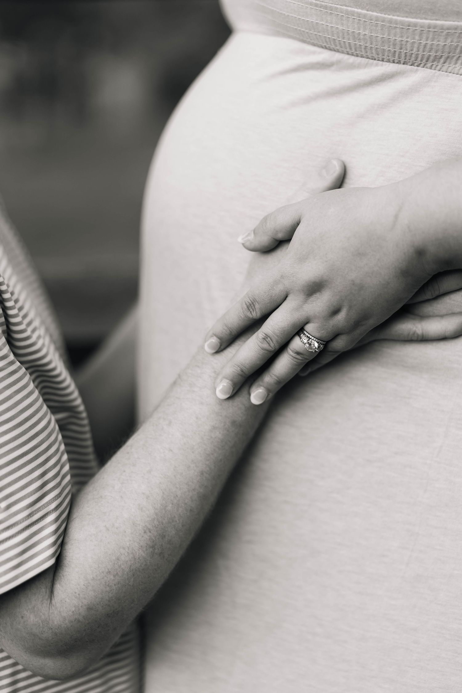 Black and white close-up of a couple's hands resting on a pregnant belly with an engagement ring in Philadelphia, PA.