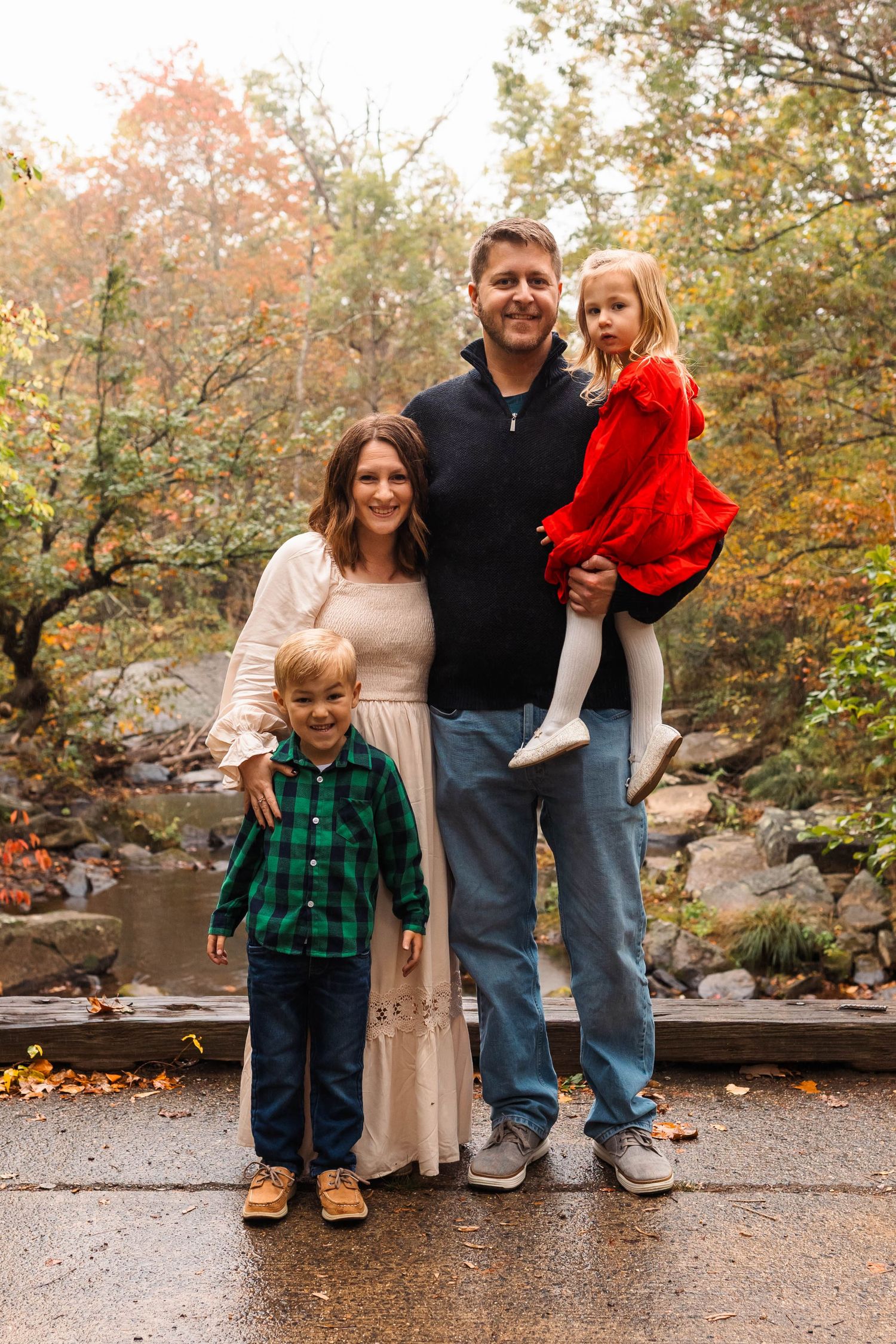 A happy family of four poses together on a rainy day in a colorful autumn park setting in Pottstown, PA.