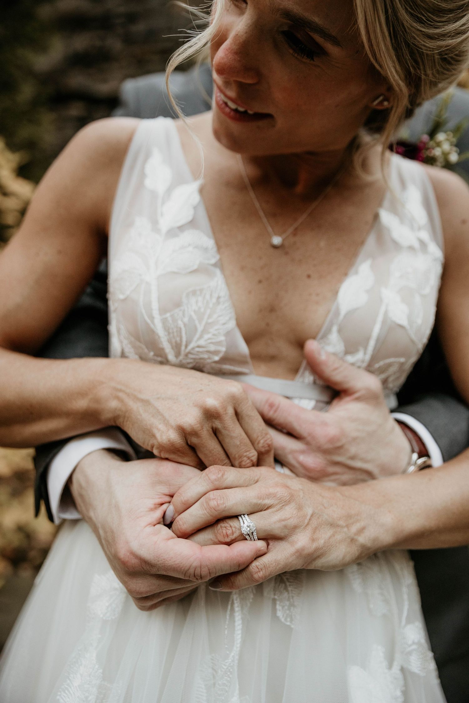 Bride and groom hold hands showing wedding rings in a tender outdoor ceremony moment.