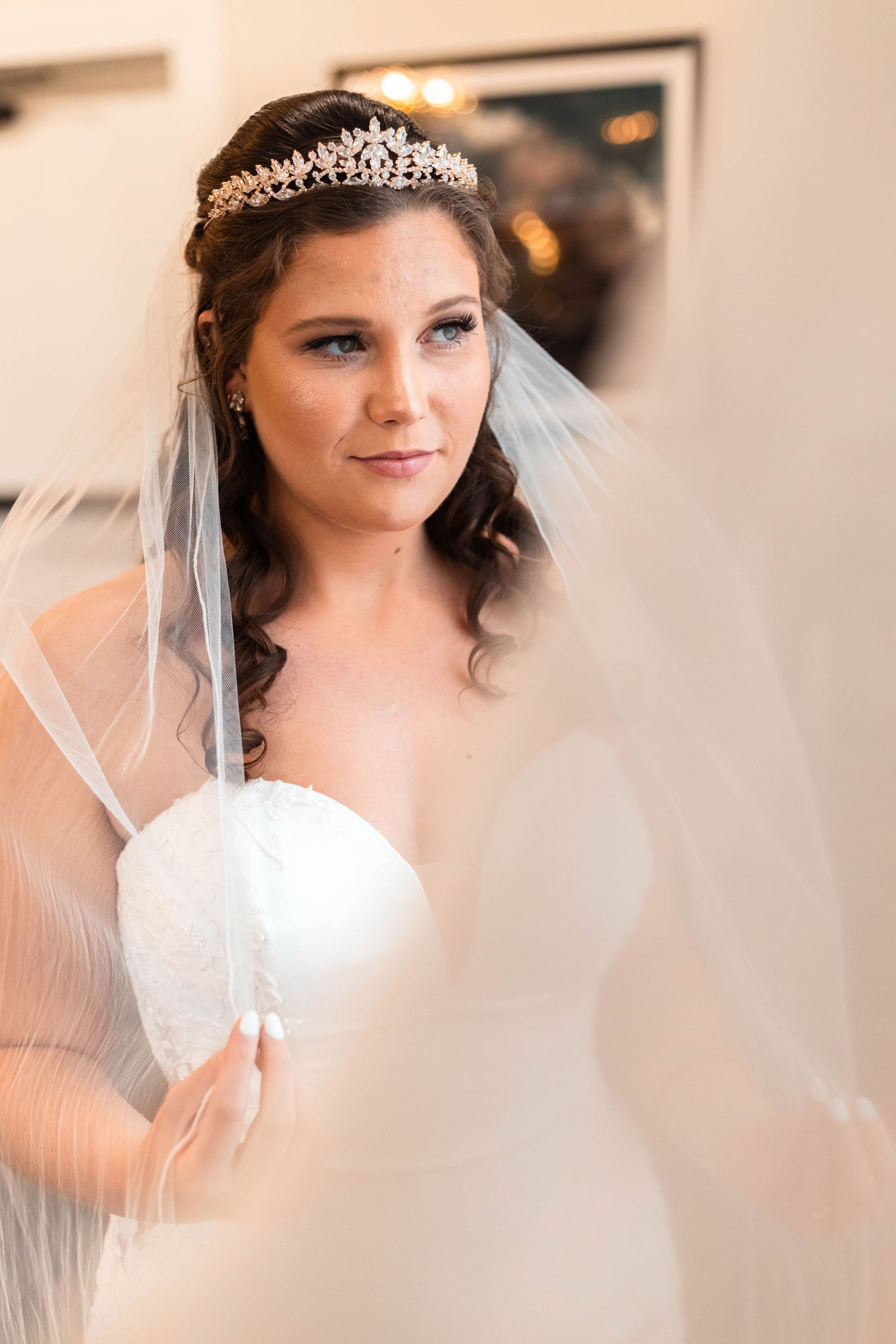 Elegant bride wearing tiara and veil holding bouquet in soft natural light during bridal portrait session.