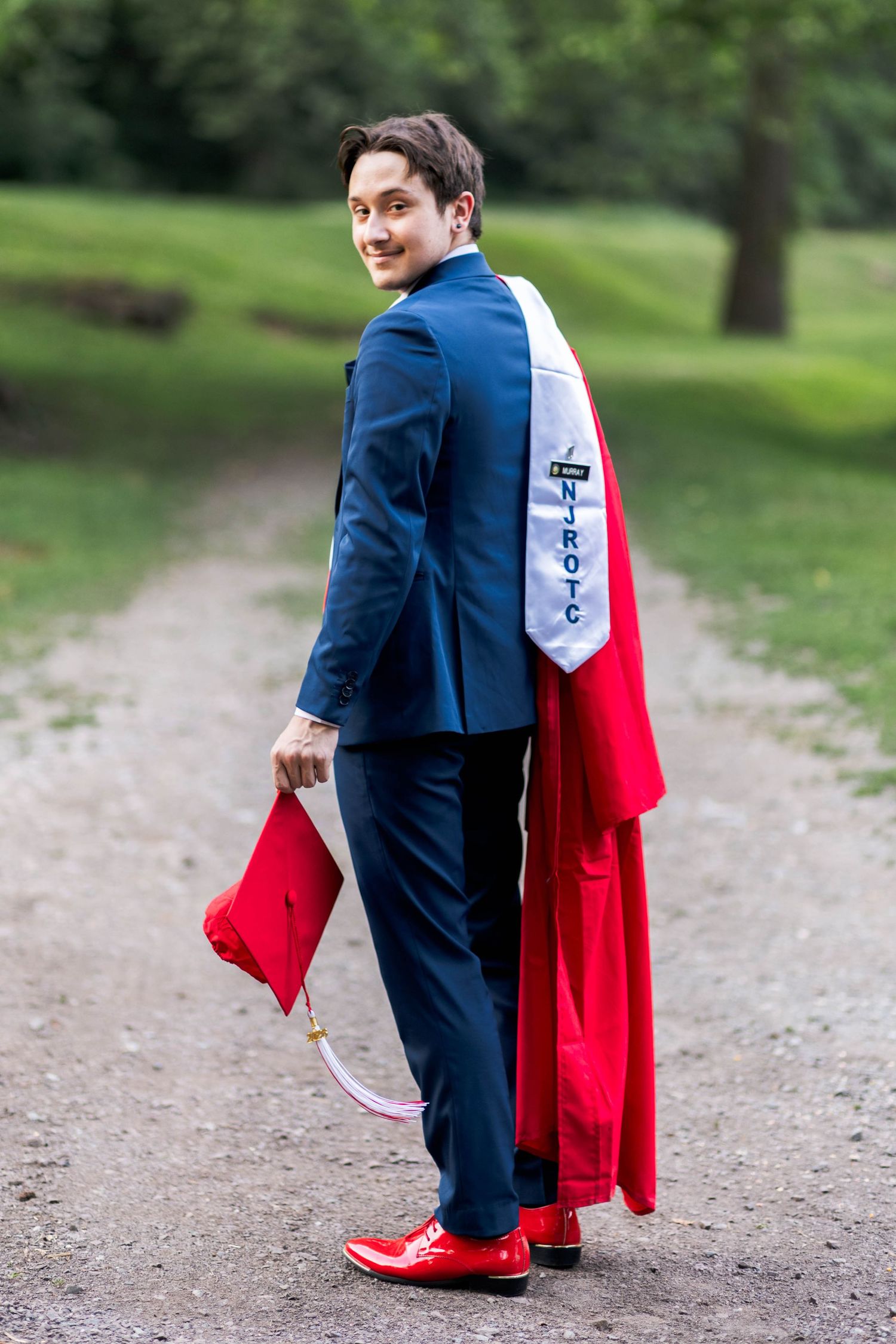 Owen J Roberts High School Graduate in blue suit with red graduation gown and stole walking on park path.