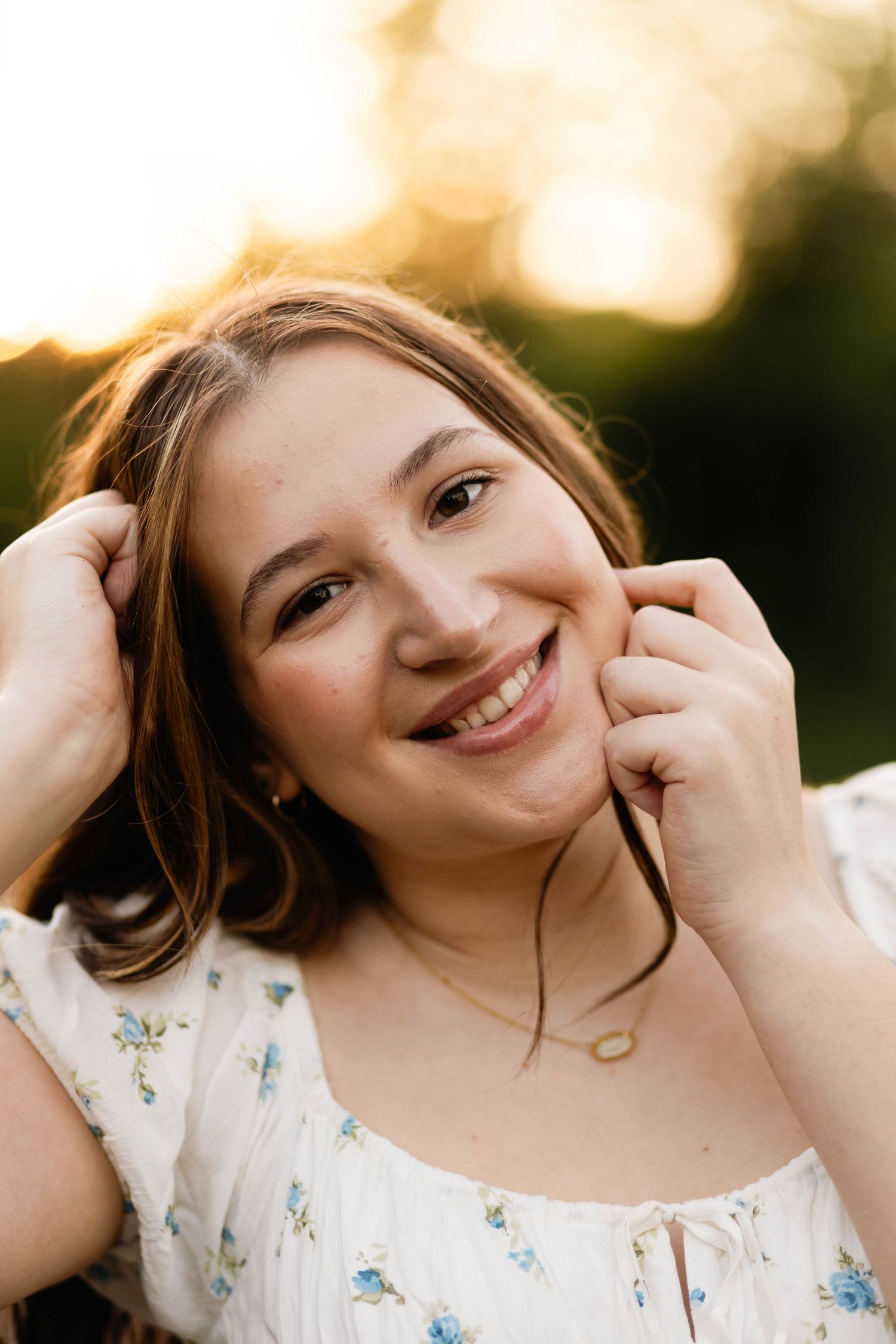 Smiling Boyertown Senior with golden sunset bokeh background in floral white dress in Harleysville, PA.