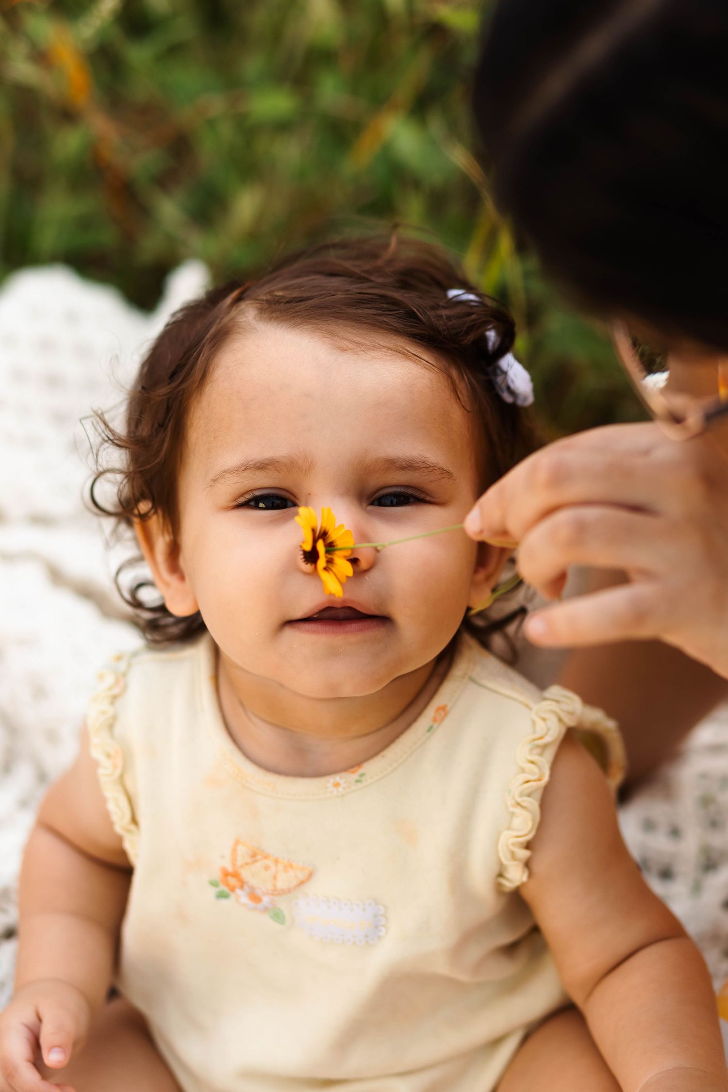 Adorable baby girl with a yellow flower on her nose held by her mother outdoors in Pekriomenville, PA.