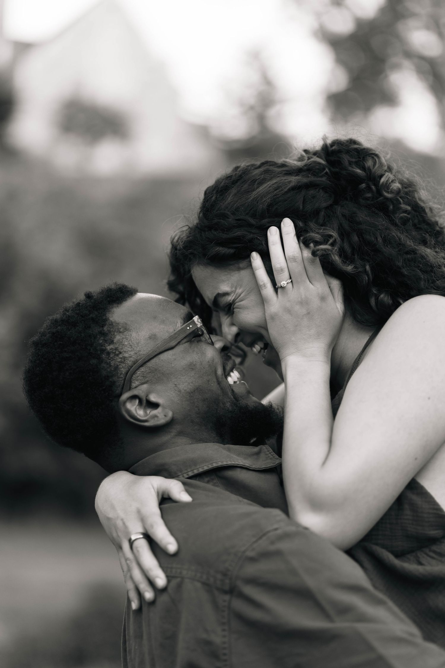 Black and white photo of joyful couple embracing, woman showing engagement ring while laughing at Grings Mill in Reading, PA.