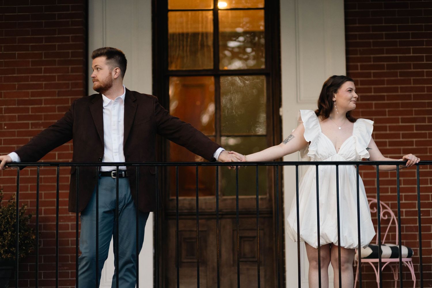 Couple standing apart on a brick porch railing, gazing outward at a historic building in West Chester, PA.