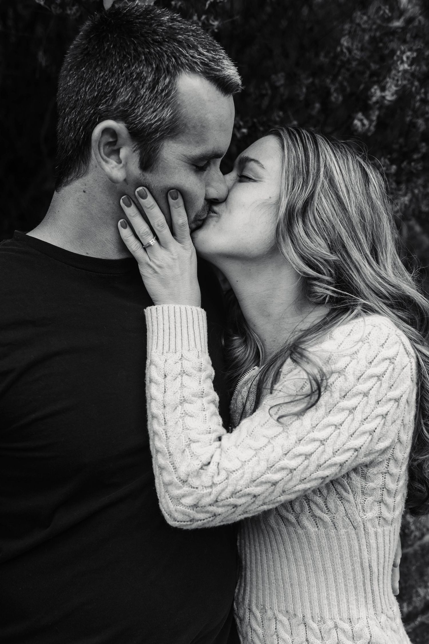 Black and white photo of a couple sharing a romantic kiss, woman wearing engagement ring and cable knit sweater in Boyertown, PA.
