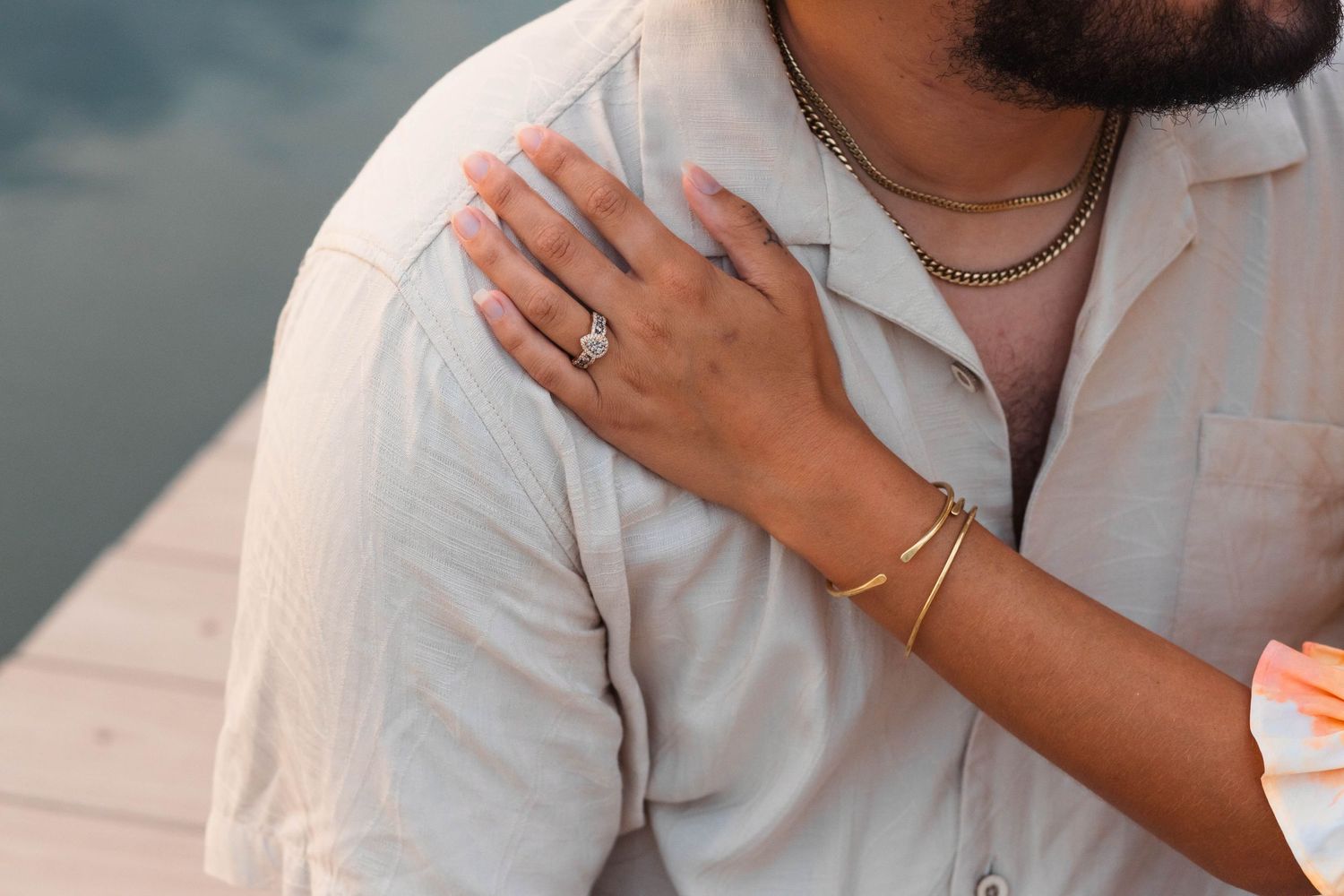 Close-up of a woman's hand with engagement ring resting on a man's shoulder near water in Elverson, PA.