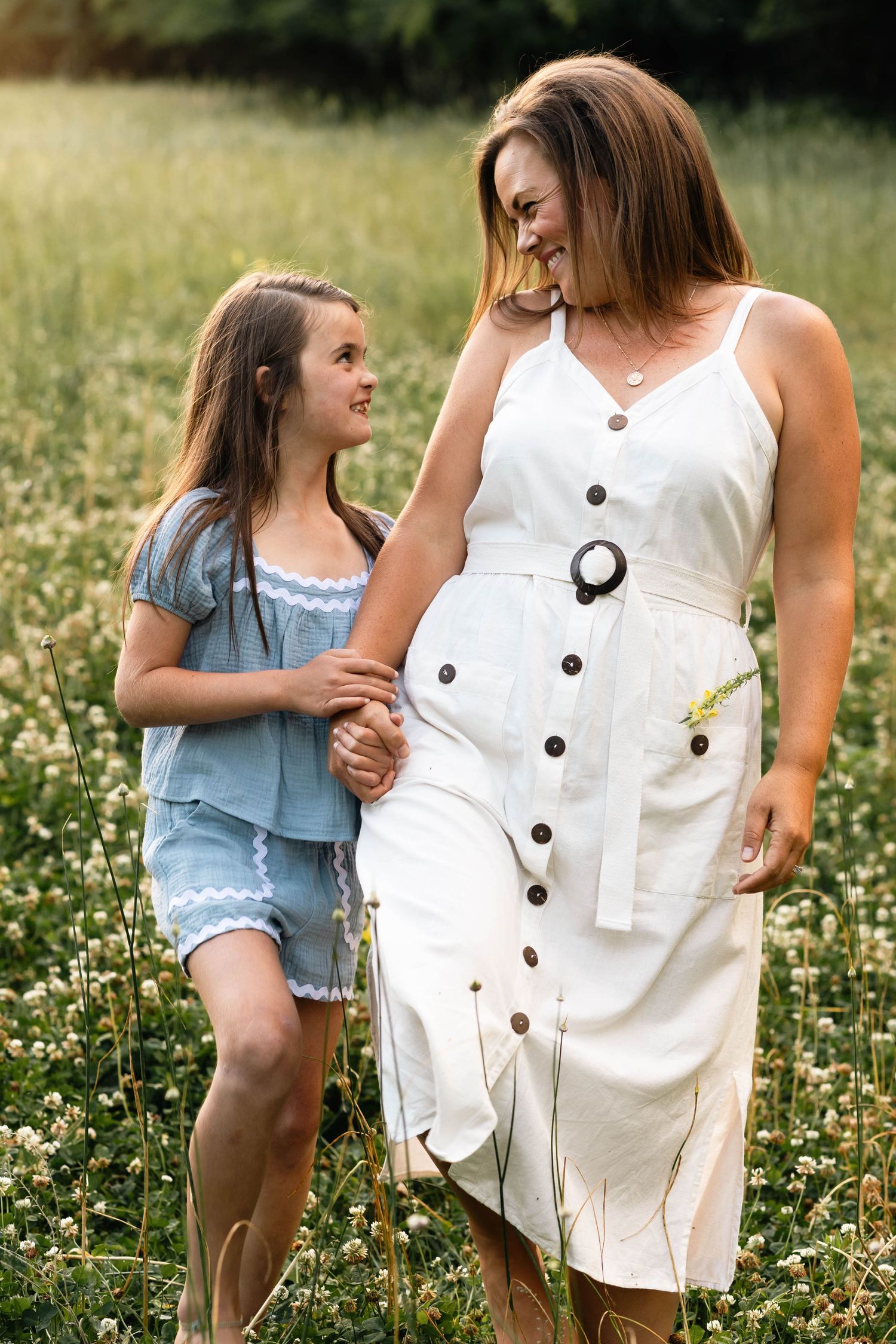 Mother and daughter holding hands and smiling at each other in a wildflower meadow in Boyertown, PA.