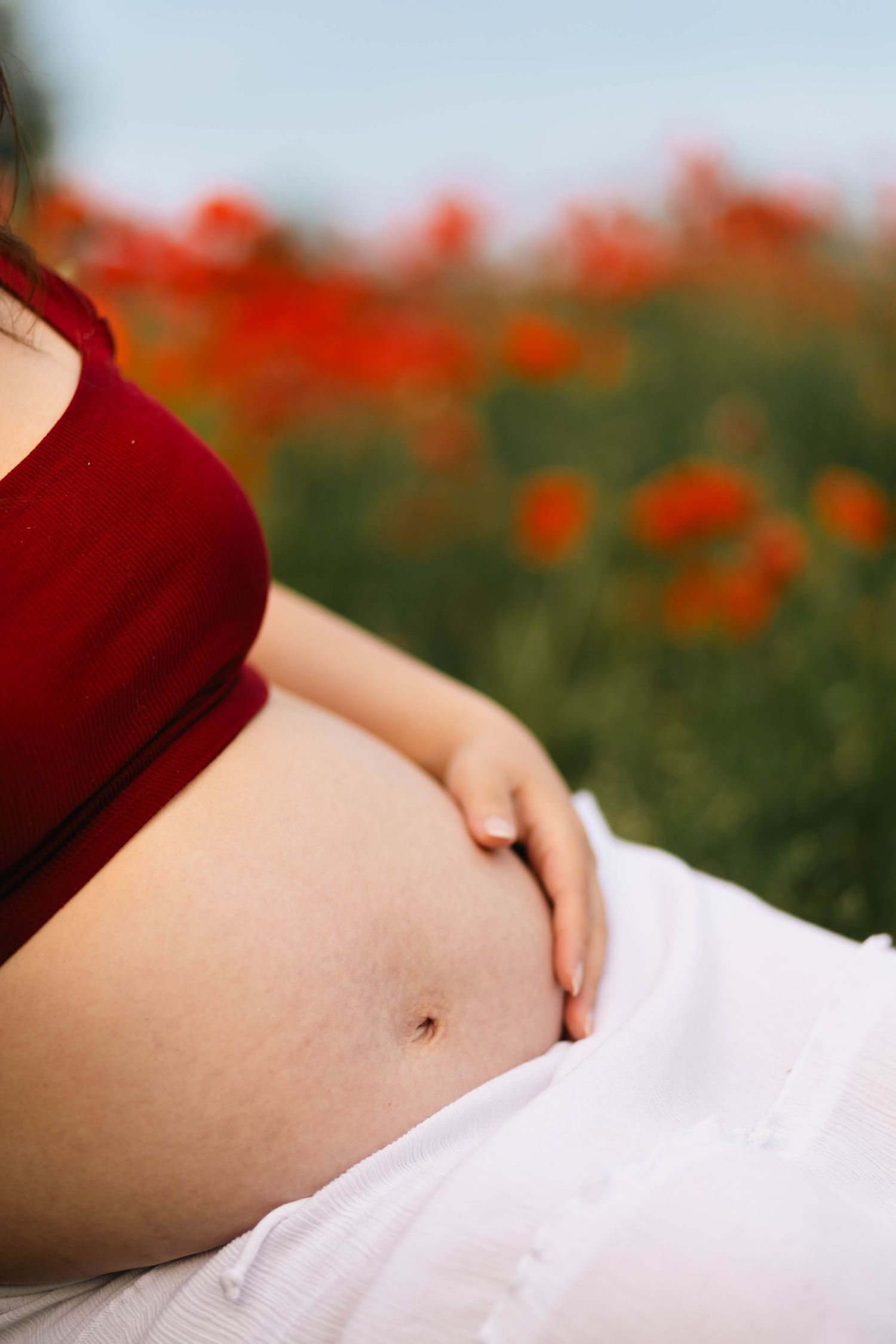 Close-up of a pregnant woman's bare belly as she rests in a field of red poppies in bloom in Douglassville, PA.