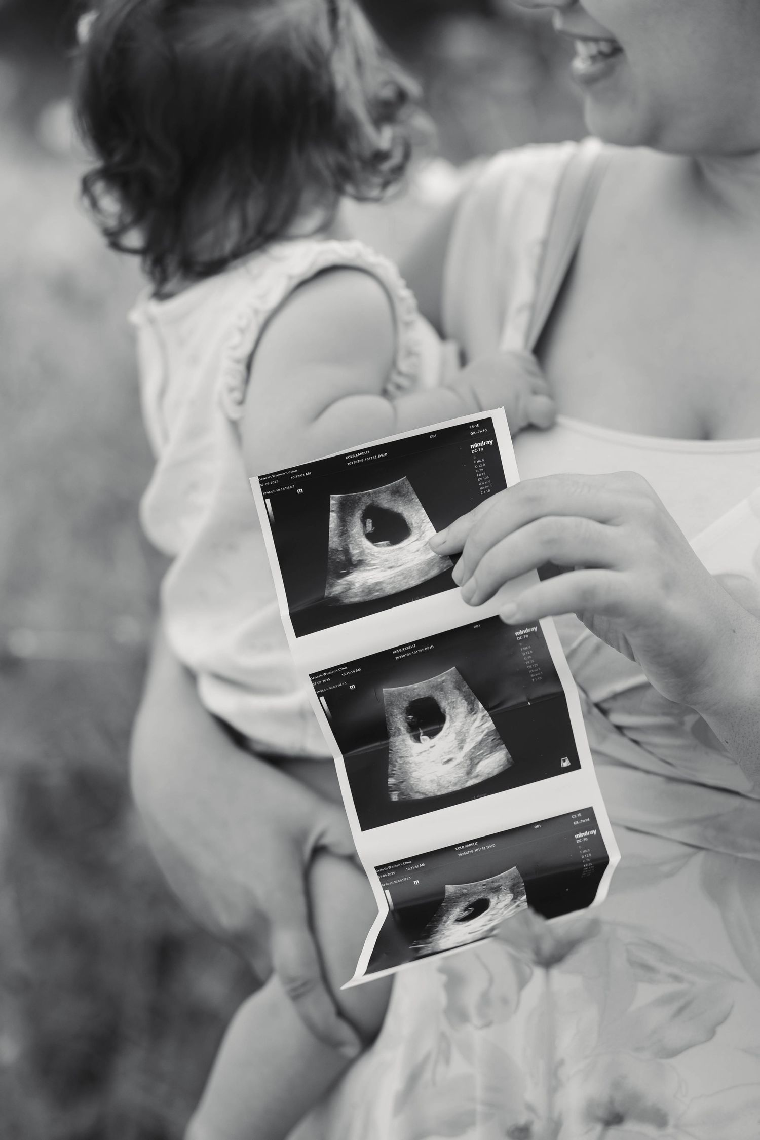 Black and white photo of parents holding toddler and ultrasound photos outdoors in Perkiomenville, PA.