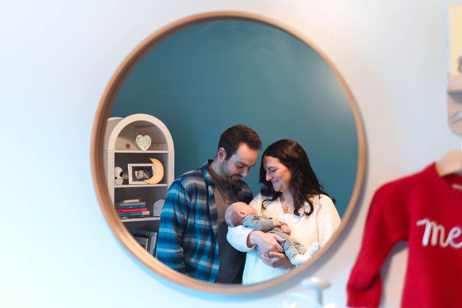 New parents admiring their newborn baby reflected in a round nursery mirror during an at home newborn session in Pottstown, PA.