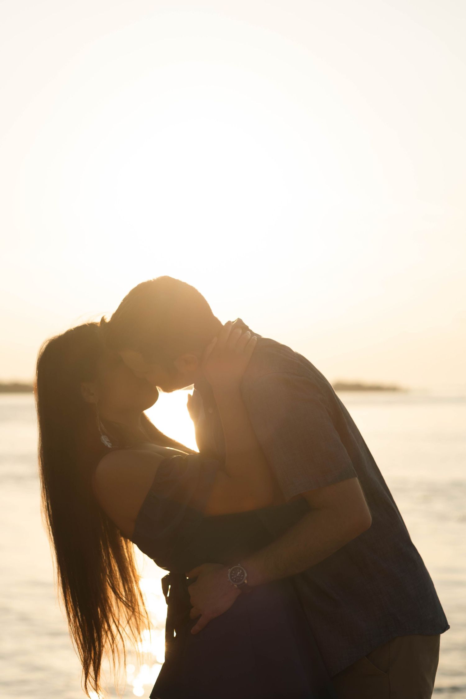 Silhouette of a couple kissing against a glowing golden sunset over the water in Barnegat, NJ.