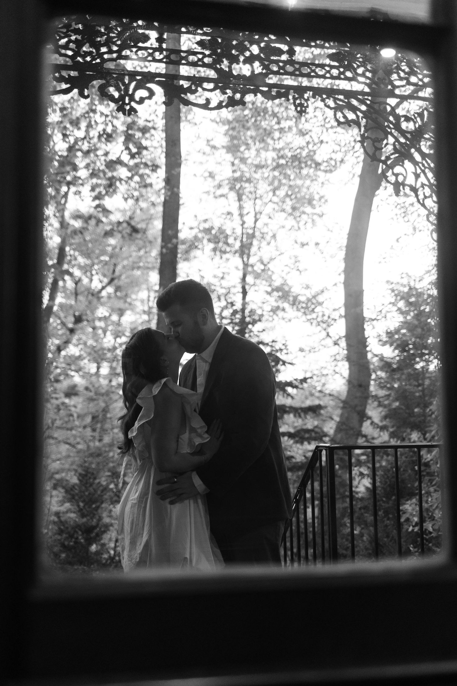 Black and white silhouette of couple kissing on balcony framed by ornate window ironwork in West Chester, PA.