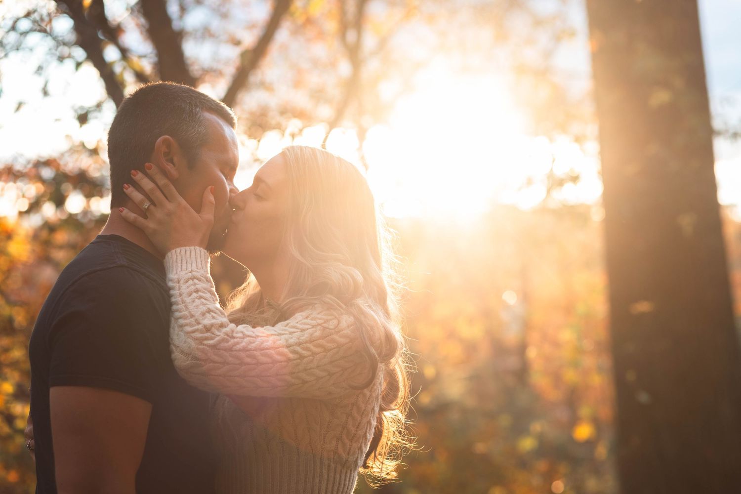 Romantic couple kissing in golden sunlight surrounded by autumn trees in an outdoor park setting in Boyertown, PA.