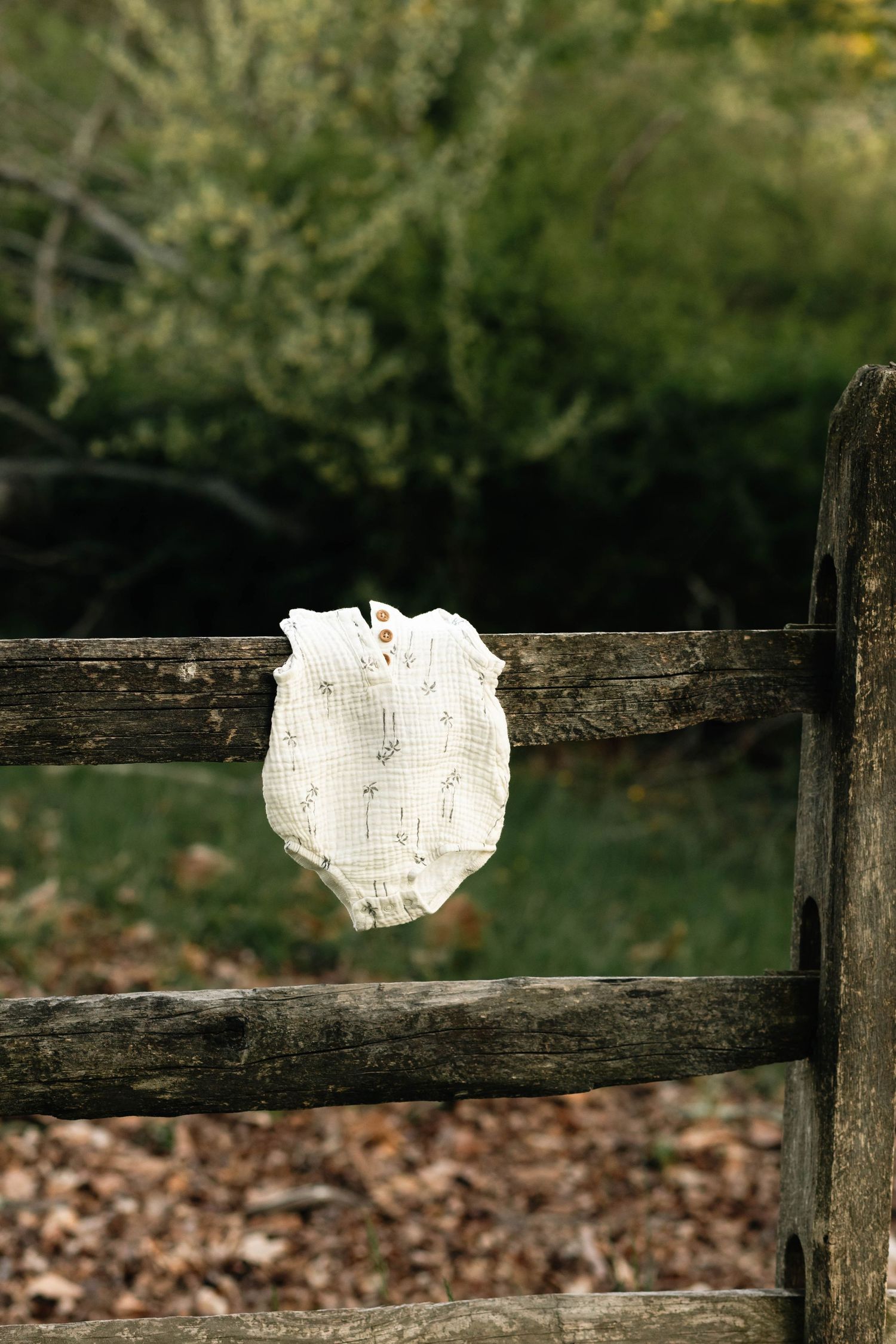 Delicate white baby onesie draped over a rustic wooden fence in an outdoor autumn setting at Hopewell Furnace in Elverson, PA.
